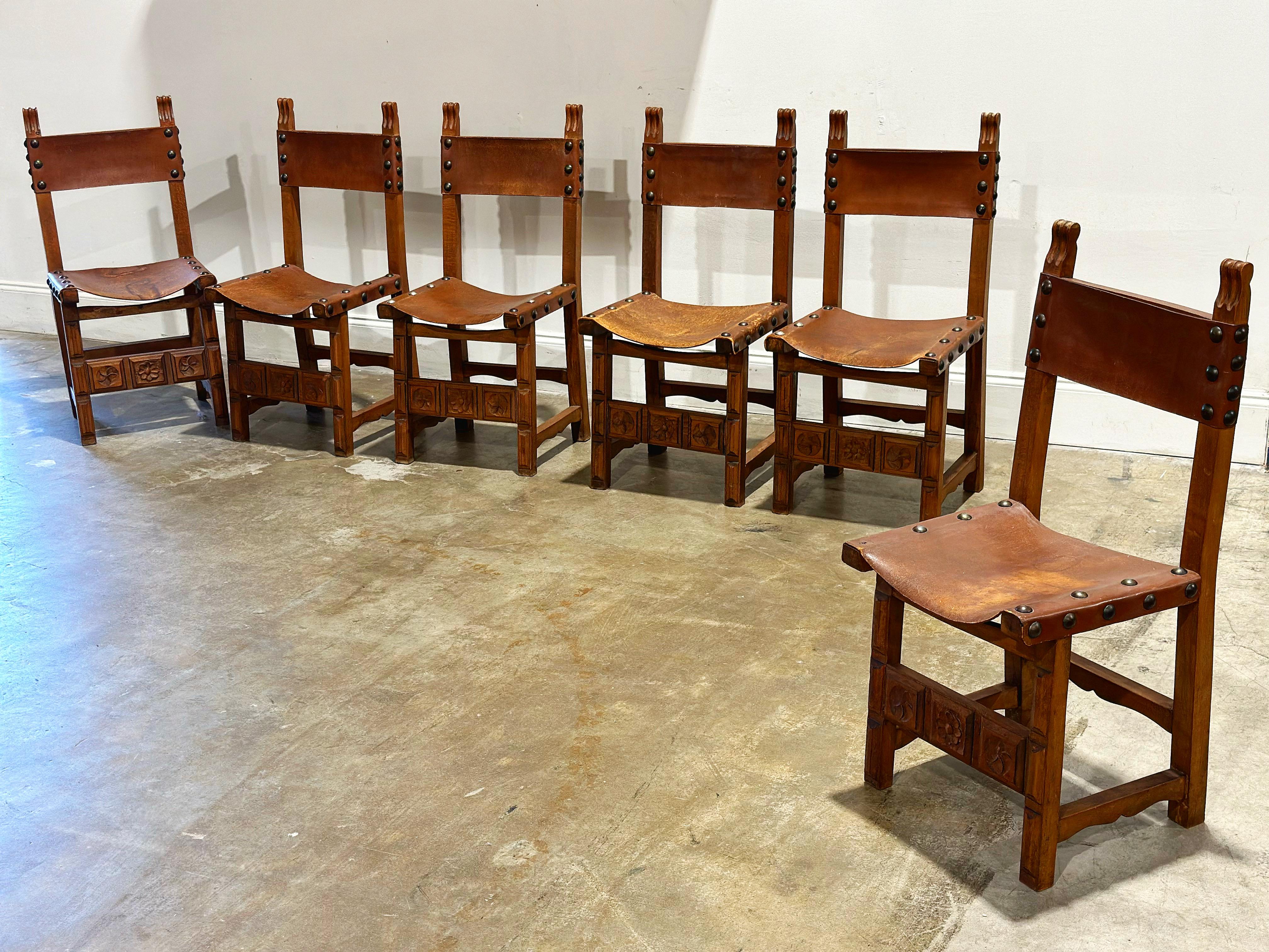 Set of 6 midcentury Spanish Revival style Brutalist dining chairs. Leather seat and back rest on heavy carved oak frames. Steel studs. In impressive original condition with minor wear. Frames are sound and sturdy. Leather seats and backs display a