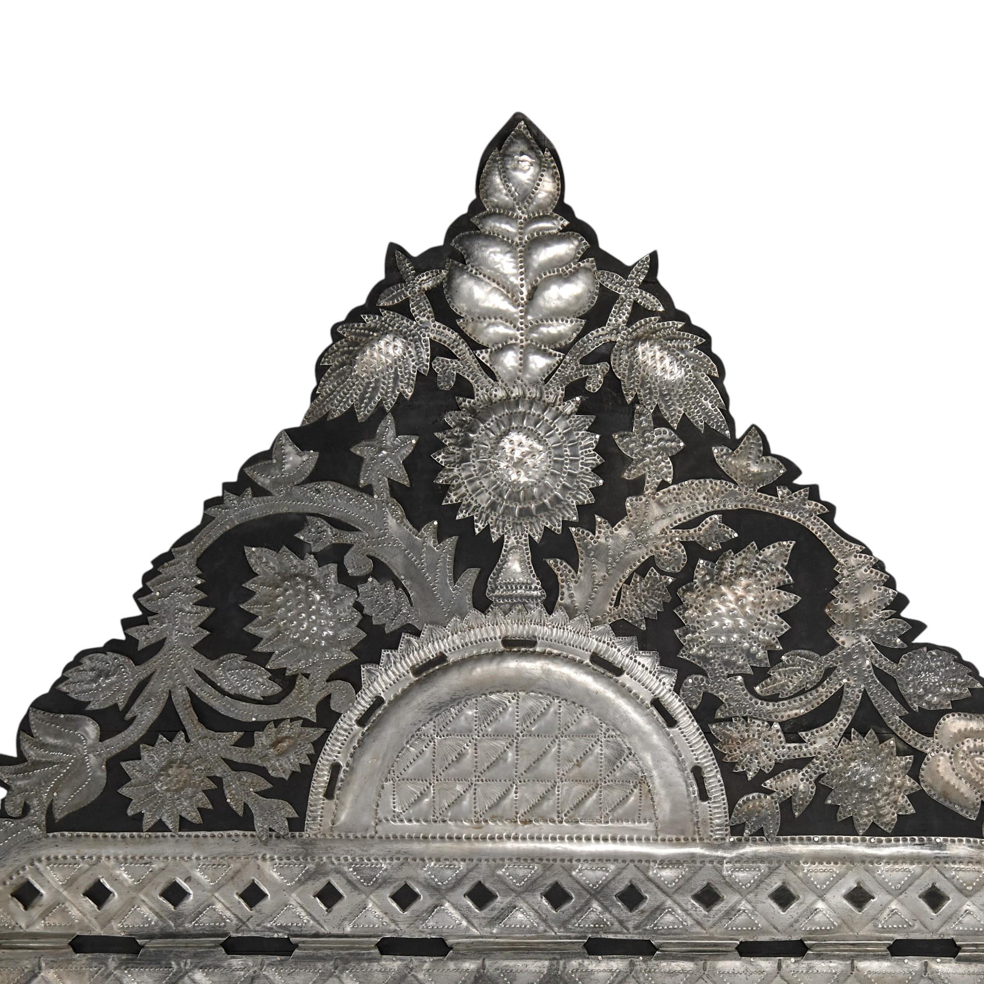 Lofty Spanish Colonial style  wall mirror with a dramatic crest decorated in hand hammered tin floral motifs over a rectangular frame having hammered quilted tin around the looking glass. 
