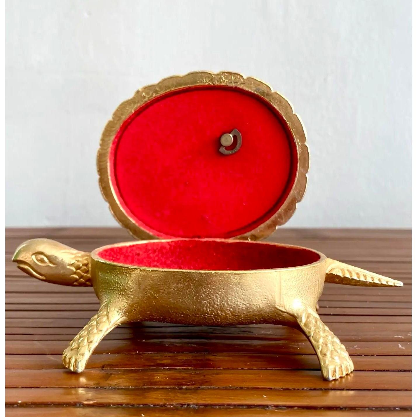 Unico e affascinante, questo portagioie vintage in ottone ha la forma di una tartaruga e presenta un'intricata raffigurazione incisa di Don Chisciotte e Sancho Panza sul guscio. L'interno è foderato di velluto rosso, perfetto per conservare piccoli