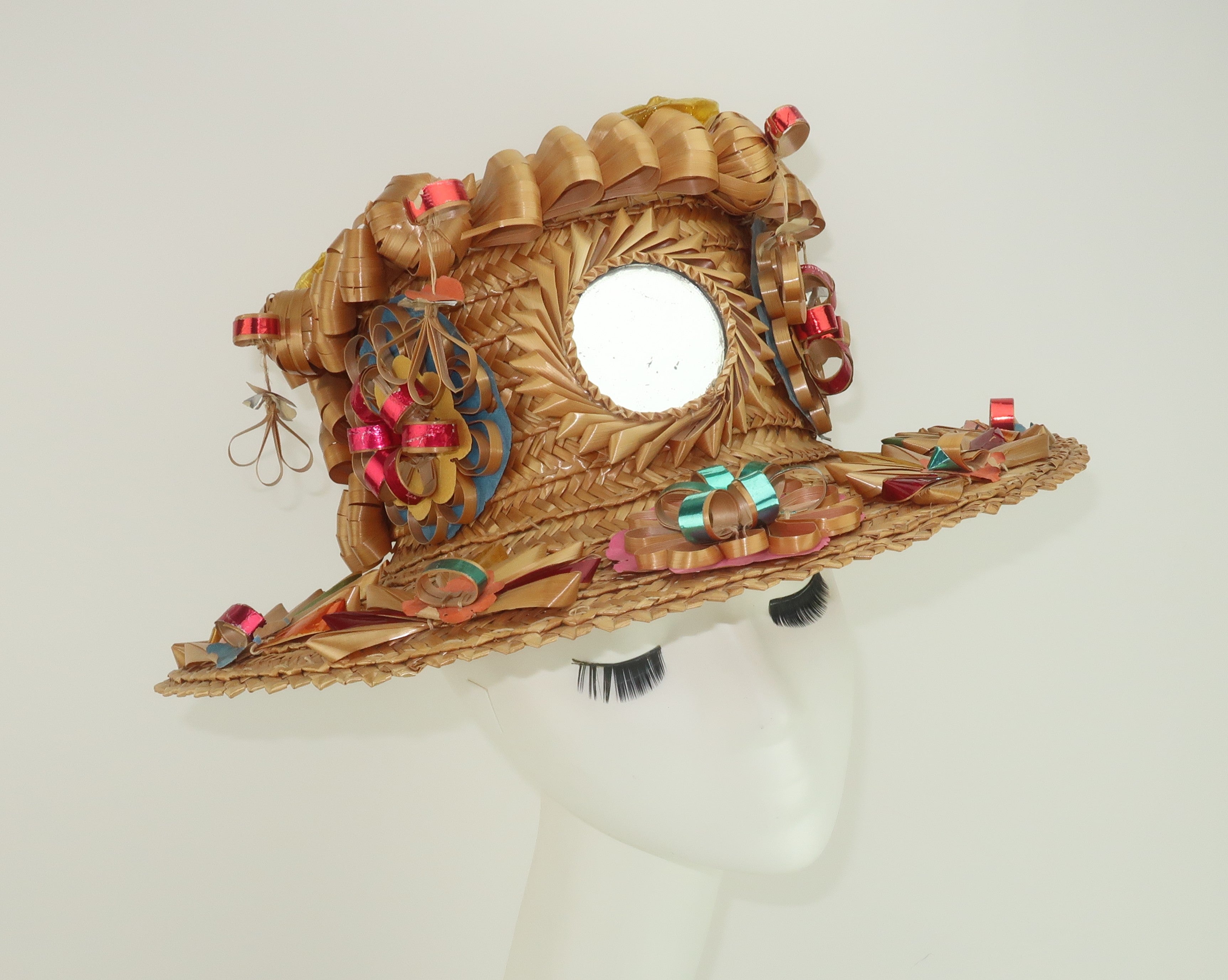 A festive straw hat embellished with curlicues, rosettes, dangles and a sun shaped mirror in the folkloric tradition of Spanish Basque country.  A closer look at the fun decor reveals foil candy and coffee labels used to form some of the curlicues. 