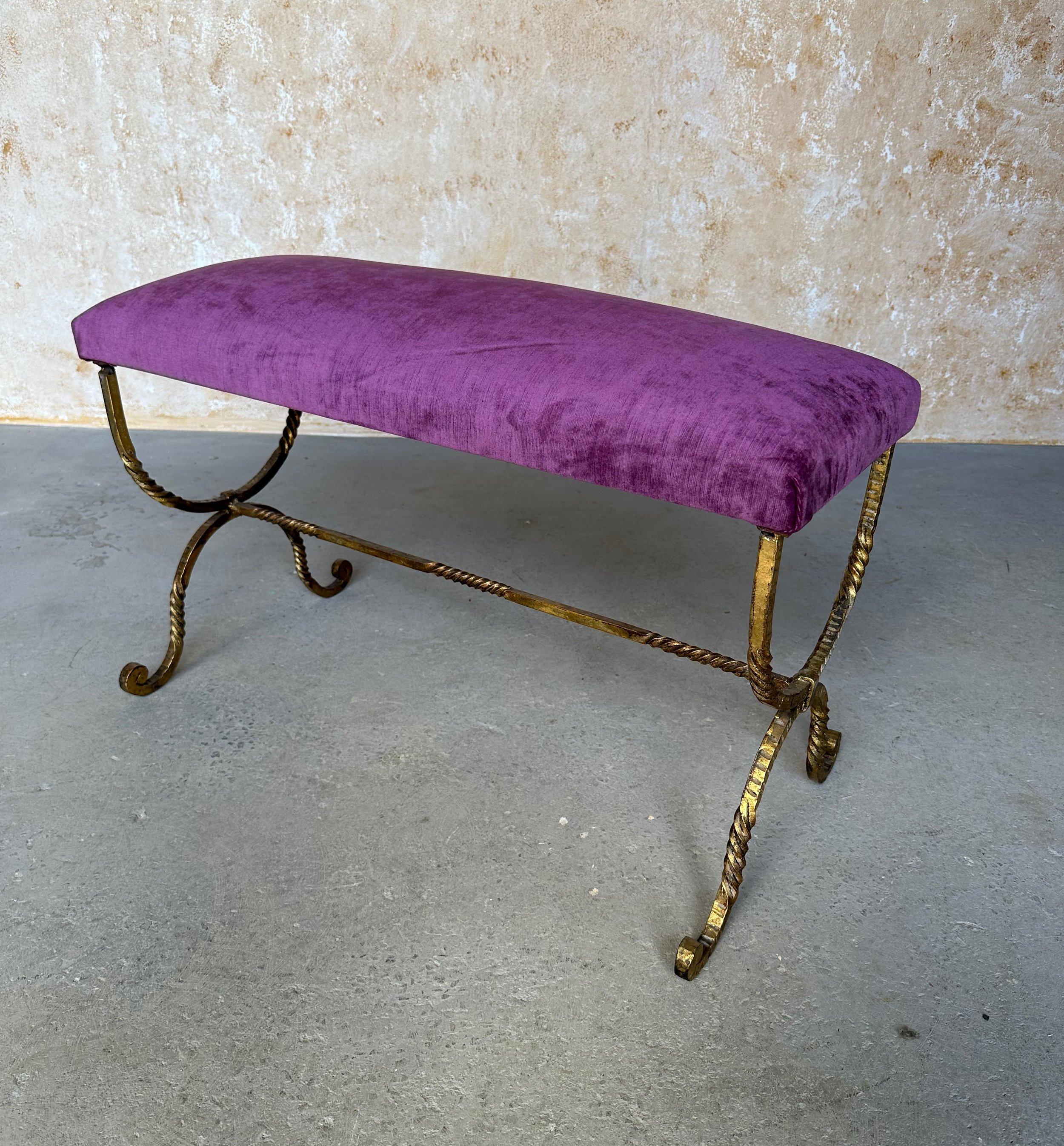 This elegant vintage 1950s Spanish gilt iron bench features an ornate, elaborately twisted hand forged hourglass frame with a decorative central stretcher and beautifully scrolled feet. The rich gilt finish is hand-applied and the seat is