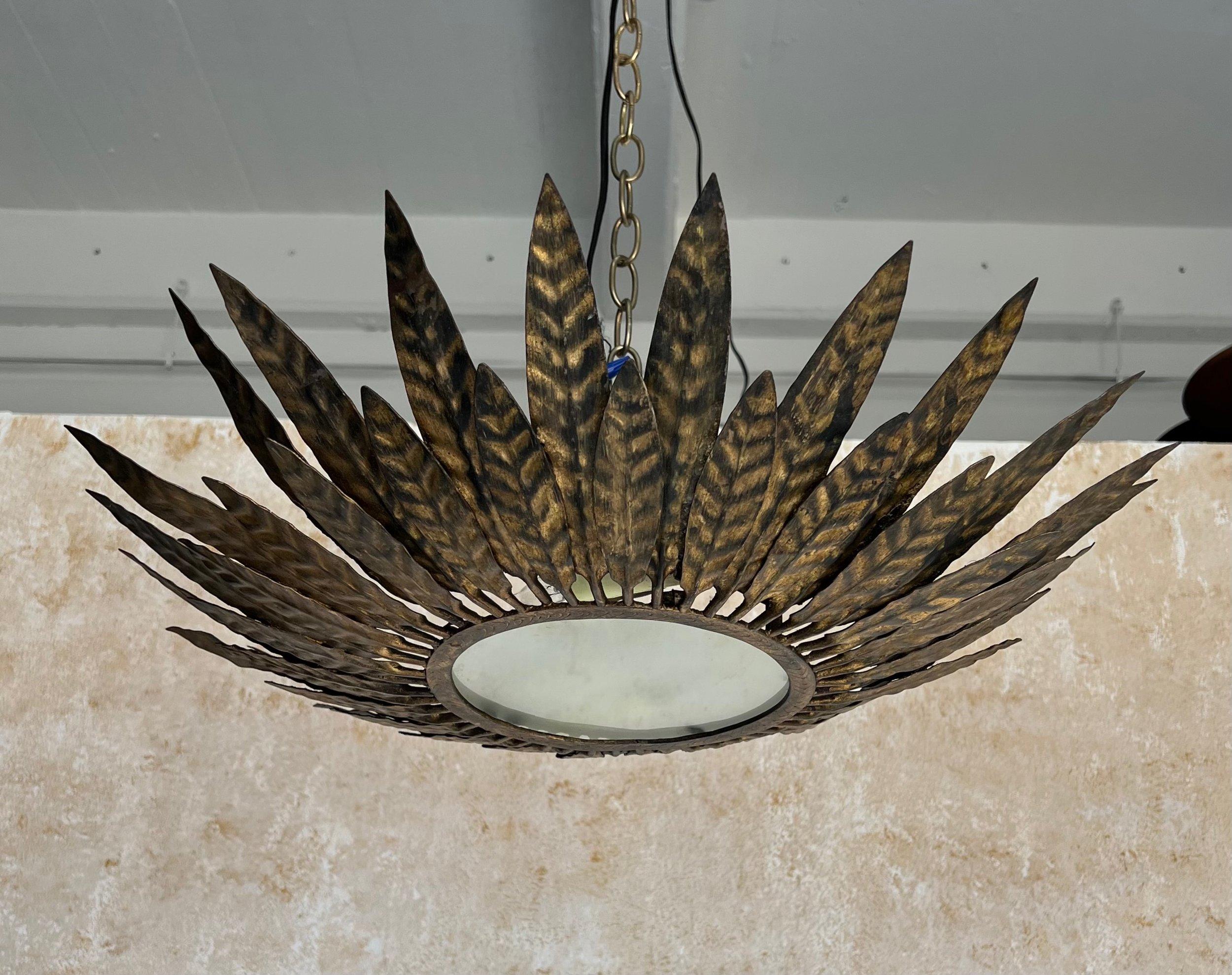 This elegant Spanish 1950s gilt metal sunburst ceiling fixture features an array of alternating and partially overlapping small and large stylized leaves emanating from a sturdy circular frame with a frosted glass center. Recently rewired to