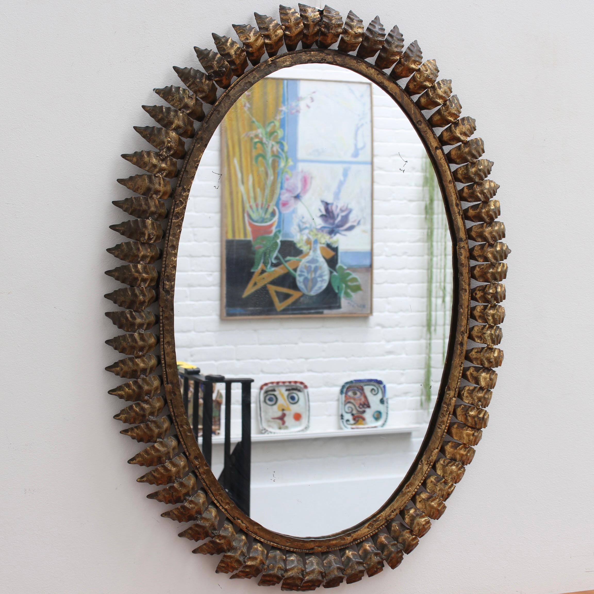 Spanischer Spiegel mit Sonnenschliff aus vergoldetem Metall (ca. 1960er Jahre) mit Blattmotiv und Strahlen. Eine authentische, gealterte Patina mit charakteristischen Markierungen auf der vergoldeten Oberfläche unterstreicht seine Präsenz und