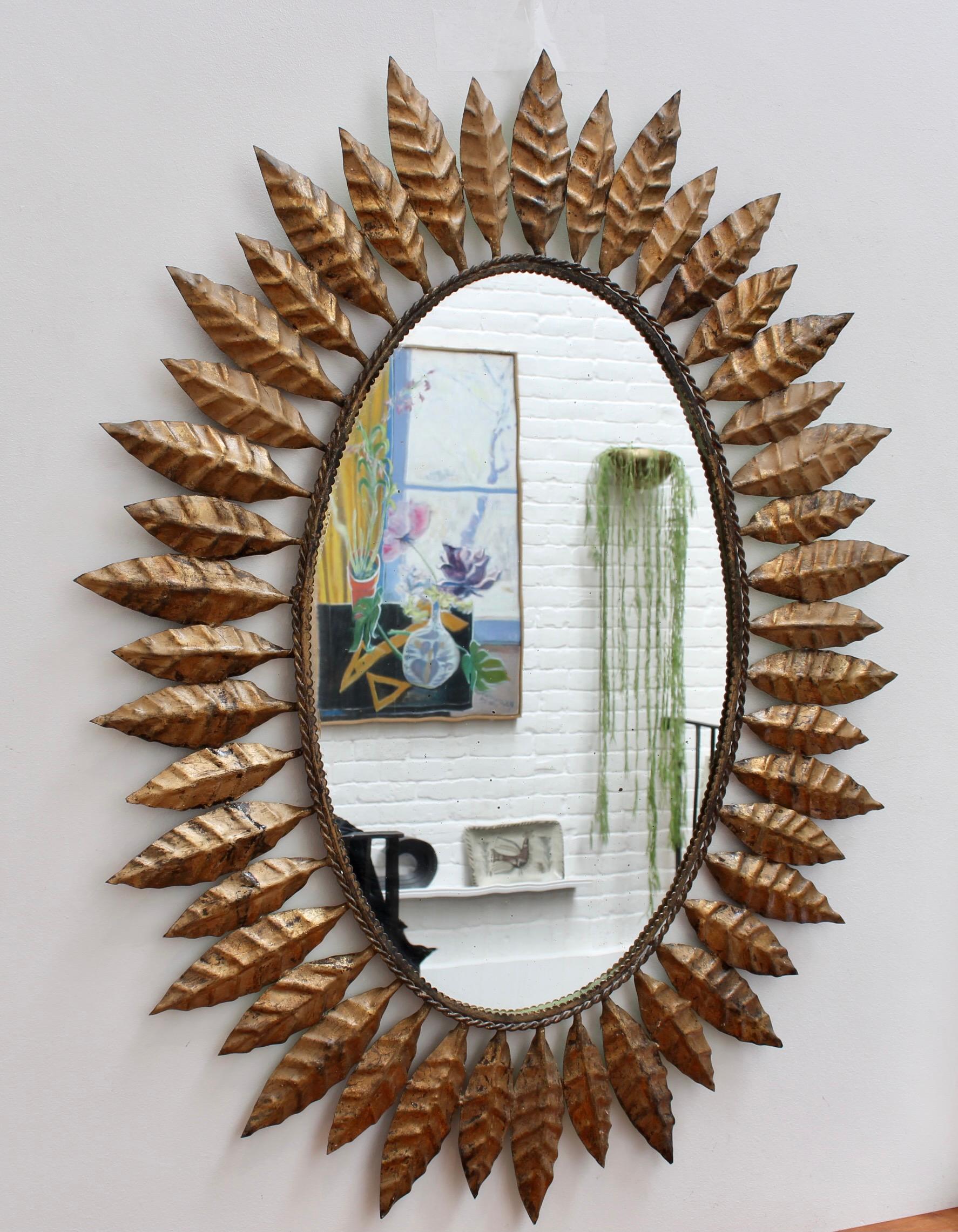 Spanish gilt tôle sunburst mirror (c. 1970s) with leaf motif and rope and wave-pattern border. The frame is in good overall condition - the glass surface has some blemishing and / or authentic age spots adding character while reflecting its true age