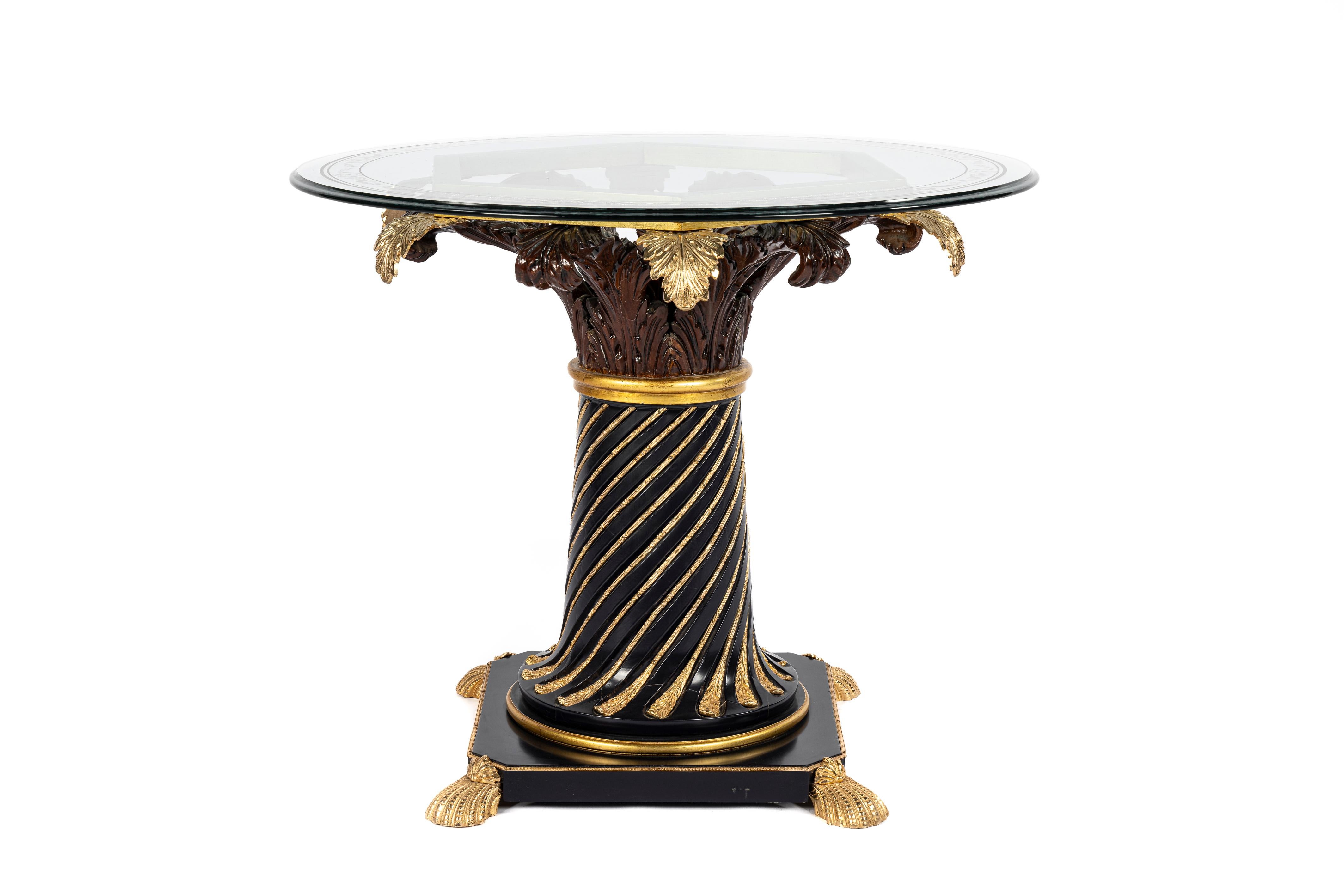 In offerta c'è un tavolo rotondo splendidamente decorato con un piano in vetro. Il tavolo presenta una base quadrata ornata da finiture in ottone e quattro piedini a forma di conchiglia agli angoli. Dalla base si erge una colonna centrale affusolata