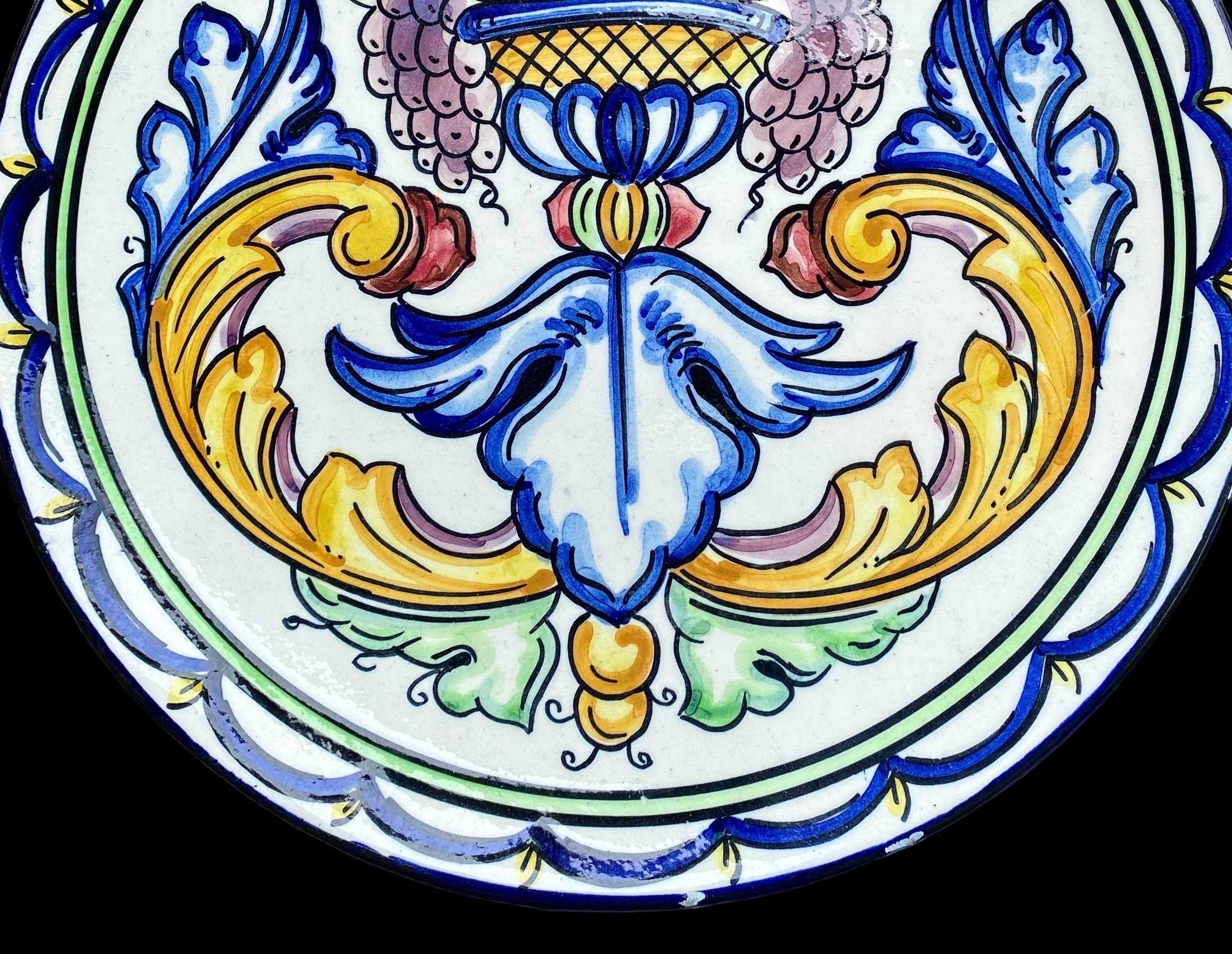 A happy, colorful and vintage Spanish majolica wall plate, representing abundance with a bowl of fruit surrounded by beautiful scrollwork, the border of blue swags and yellow pelments completes the overall design. 
Hang this in your keeping room,