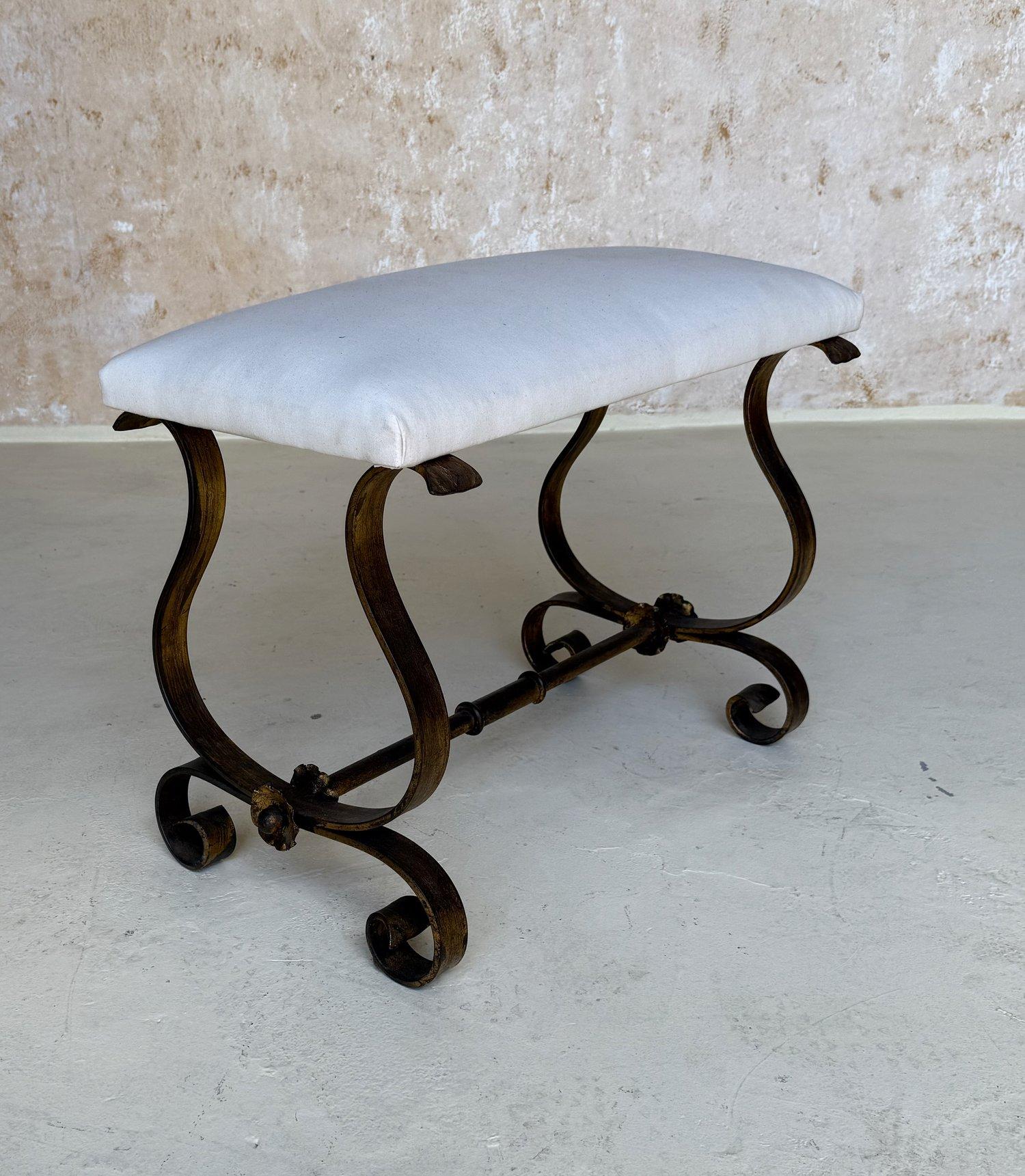 This elegant mid century Spanish gilt iron bench from the 1950s features an ornate hand forged base with elaborate scrollwork and a stretcher with decorative central ring details and florets and spheres at the ends. The rich gold gilt finish is hand