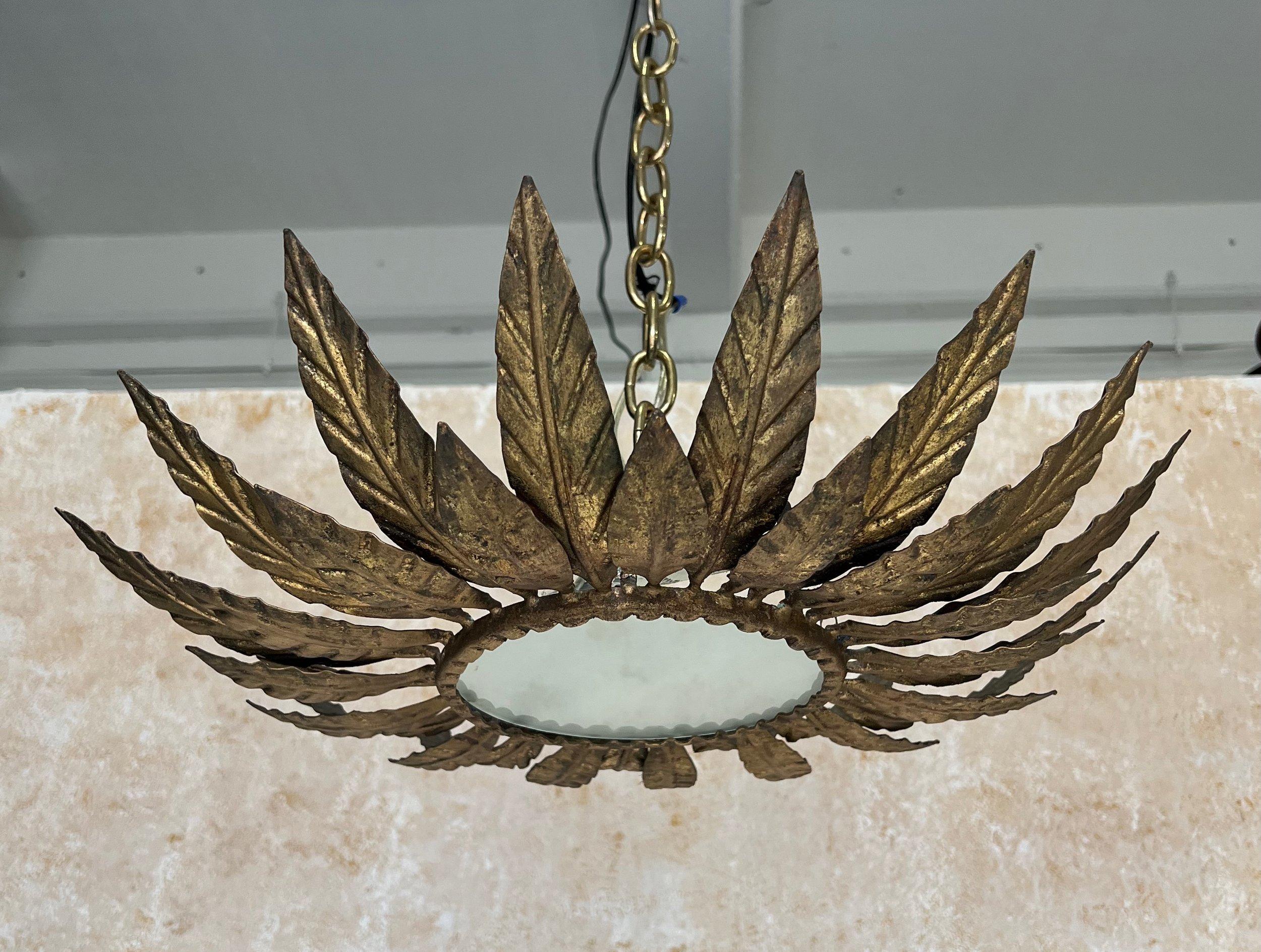 This lovely Spanish 1950s gilt metal ceiling fixture features alternating large and small partially overlapping stylized leaves surrounding a sturdy circular frame that holds the frosted glass center. The rich hand applied gold gilt patina is