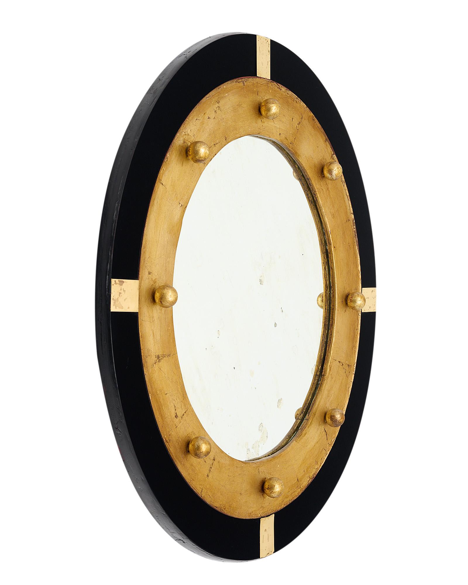 Vintage Spanish mirror with a circular central mirror and a wooden structure. This piece features gold leafing and a beautiful patina. It is framed with black glass and enhanced with small spheric gold finials and brass elements.
