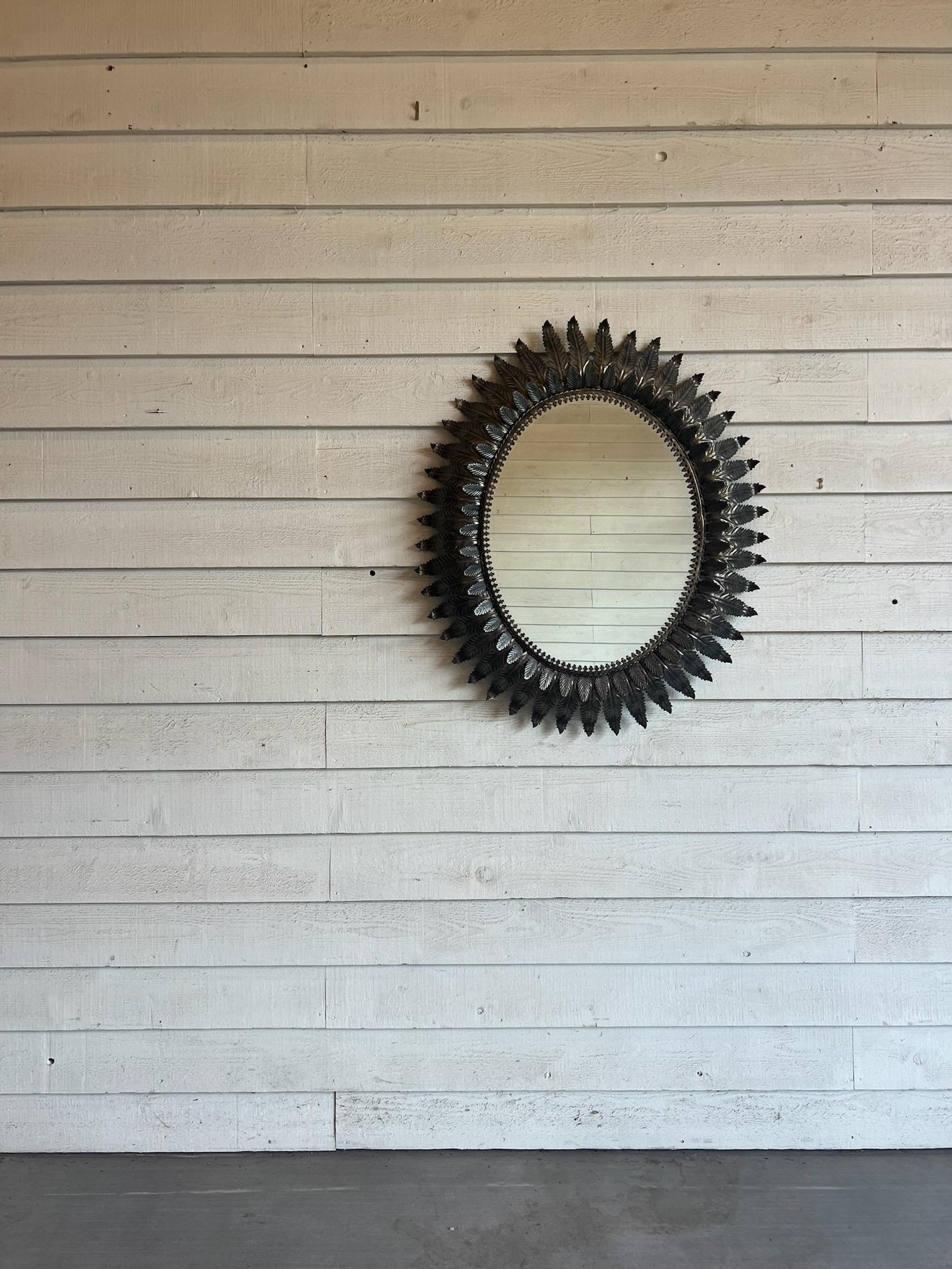 Handcrafted with exquisite detail, this oval Spanish mirror includes hand cut metal leaf detail which surrounds the mirror itself in three rows, each with the leaf in varying size. Discovered in Northern Spain near Barcelona, this mirror measures