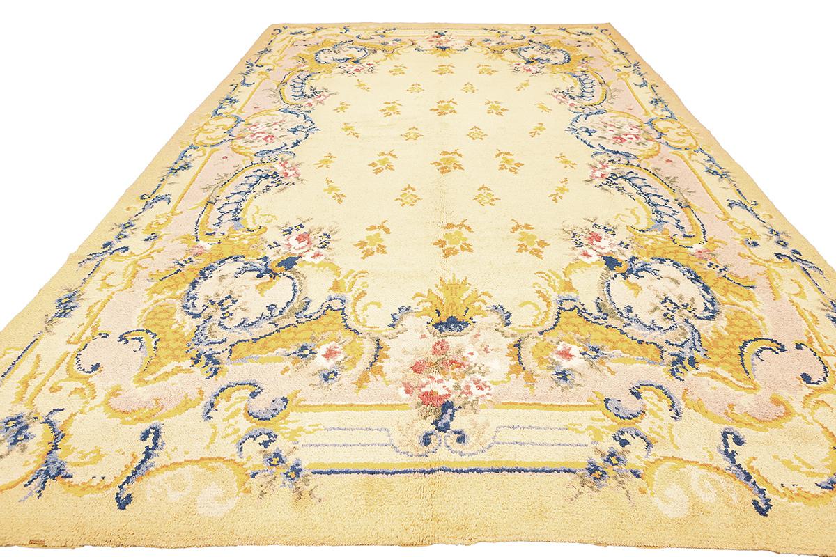 Behold the splendor of this vintage Spanish rug, a majestic piece that brings the grandeur of Spain's rich heritage to your living space. This exquisite rug is a symphony in golden yellow, adorned with intricate Rococo-inspired motifs that speak of