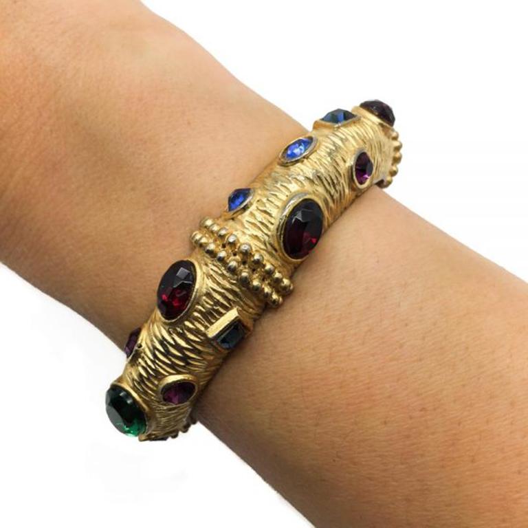 A wonderful 'gem' encrusted 1980s gold plated vintage Sphinx bangle. This signed bangle features many faux gems of differing cuts and colors including blue, green, red and purple to present an incredibly vibrant and luxurious looking piece of