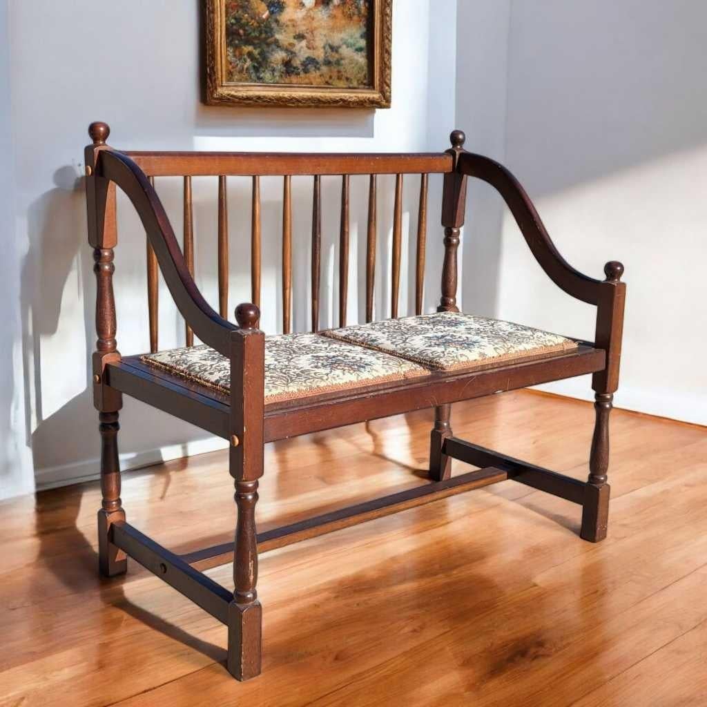 A delightful vintage spindle-back wood settee featuring gracefully curved arms, turned legs, and a floral tapestry-style upholstered seat. This compact bench blends traditional design with cozy, cottage-inspired charm—ideal for use in an entryway,