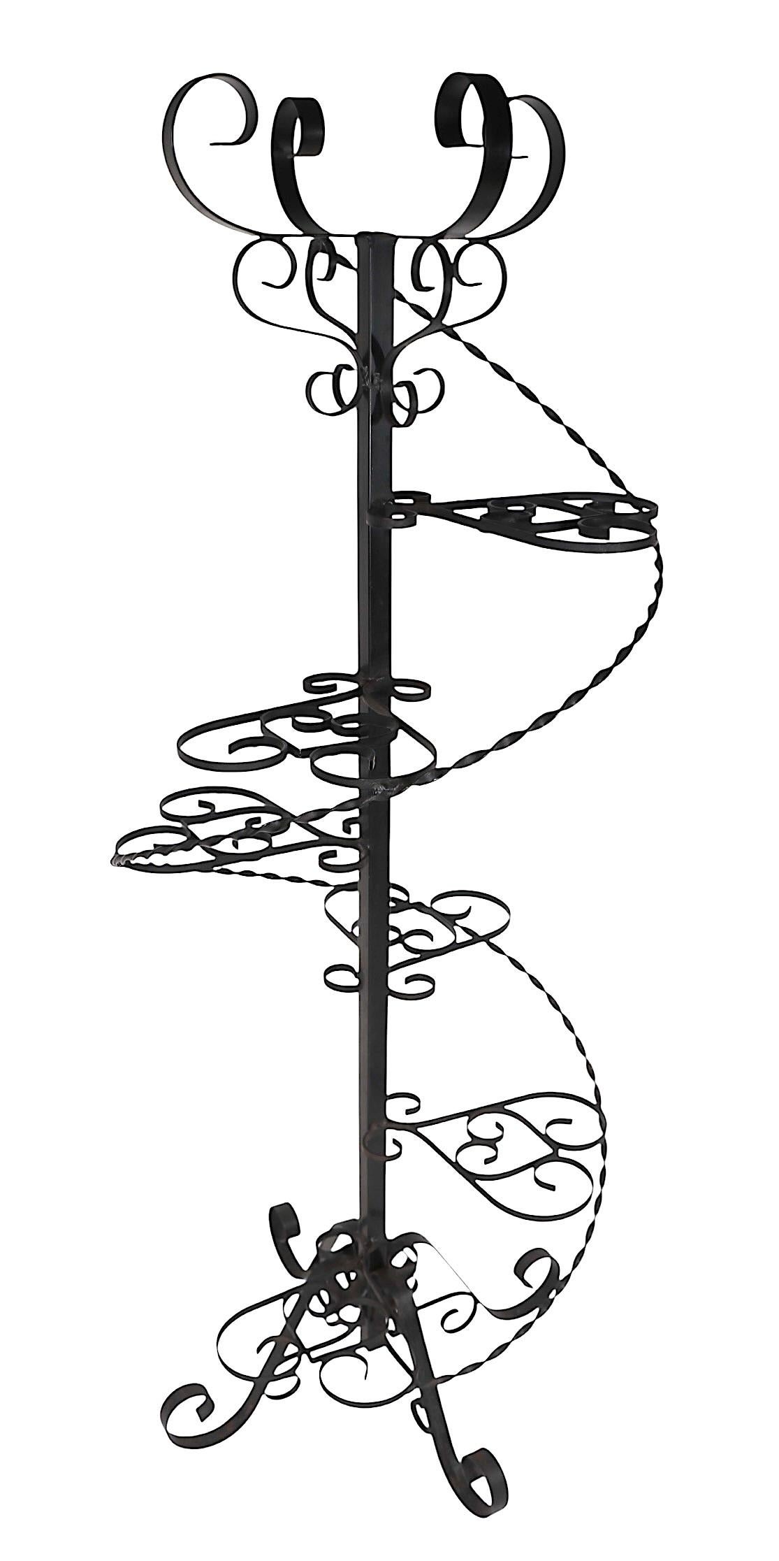 Decorative mid century  freestanding wrought iron plant stand having six stepped platform shelves, and a basket form plant holder at the top. 
 Suitable for either indoor, or outdoor use, this functional piece is a perfect addition to your sunroom,