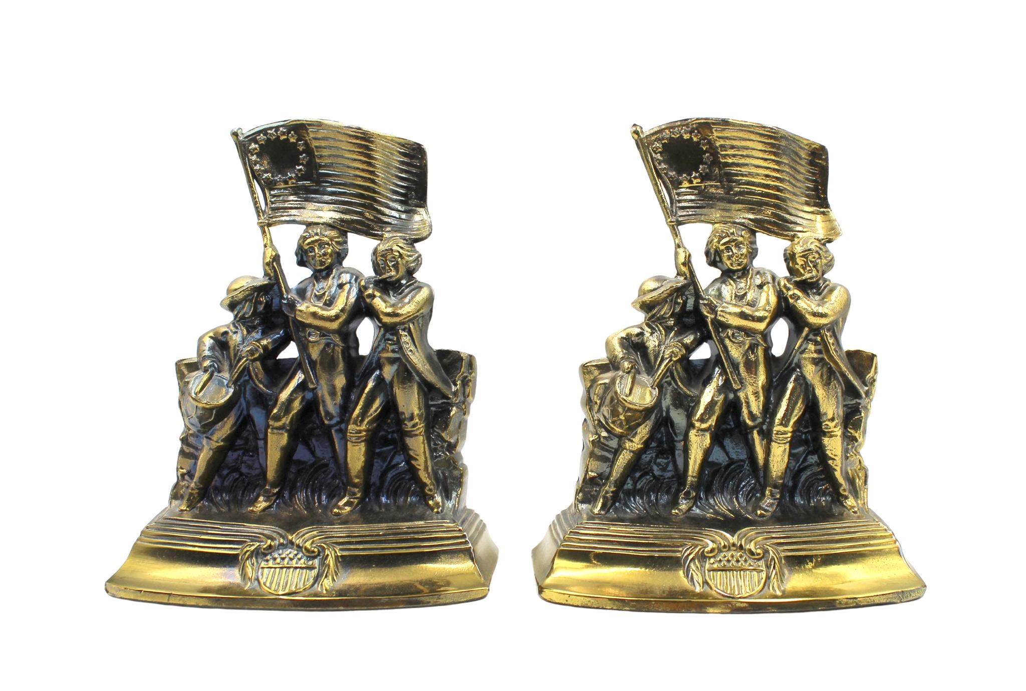 Offered is a set of vintage brass Revolutionary War soldiers bookends. Each bookend depicts a fife player, a drummer, and a flag bearer, marching in step together across a grassy field. The flag bearer hoists a large 13-star medallion flag into the