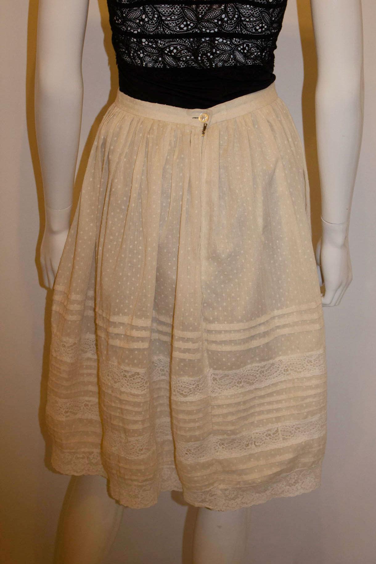 A pretty vintage cotton skirt in spot cotton with lace detail. The skirt is in an ivory colour with gathering at the waist and fold and lace detail. It  has a central back zip opening and is fully lined. 
Measurement' Waist 25'' ,length 25''.