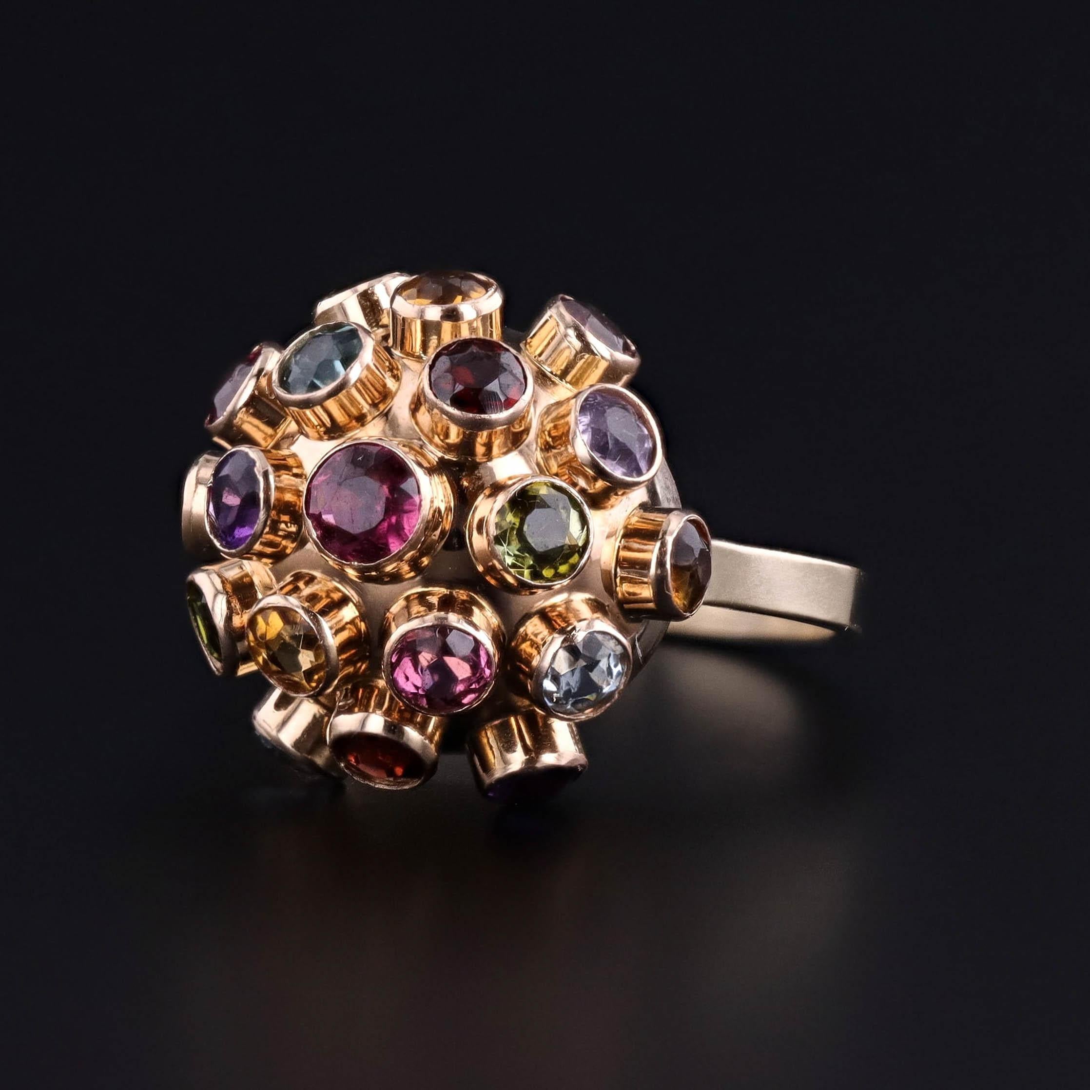 Questo anello vintage presenta un audace motivo Sputnik, con una serie di gemme colorate incastonate in un radioso oro 14k. Il design dinamico, simile a una sfera, che prende il nome dal famoso satellite sovietico del 1957, riflette il fascino