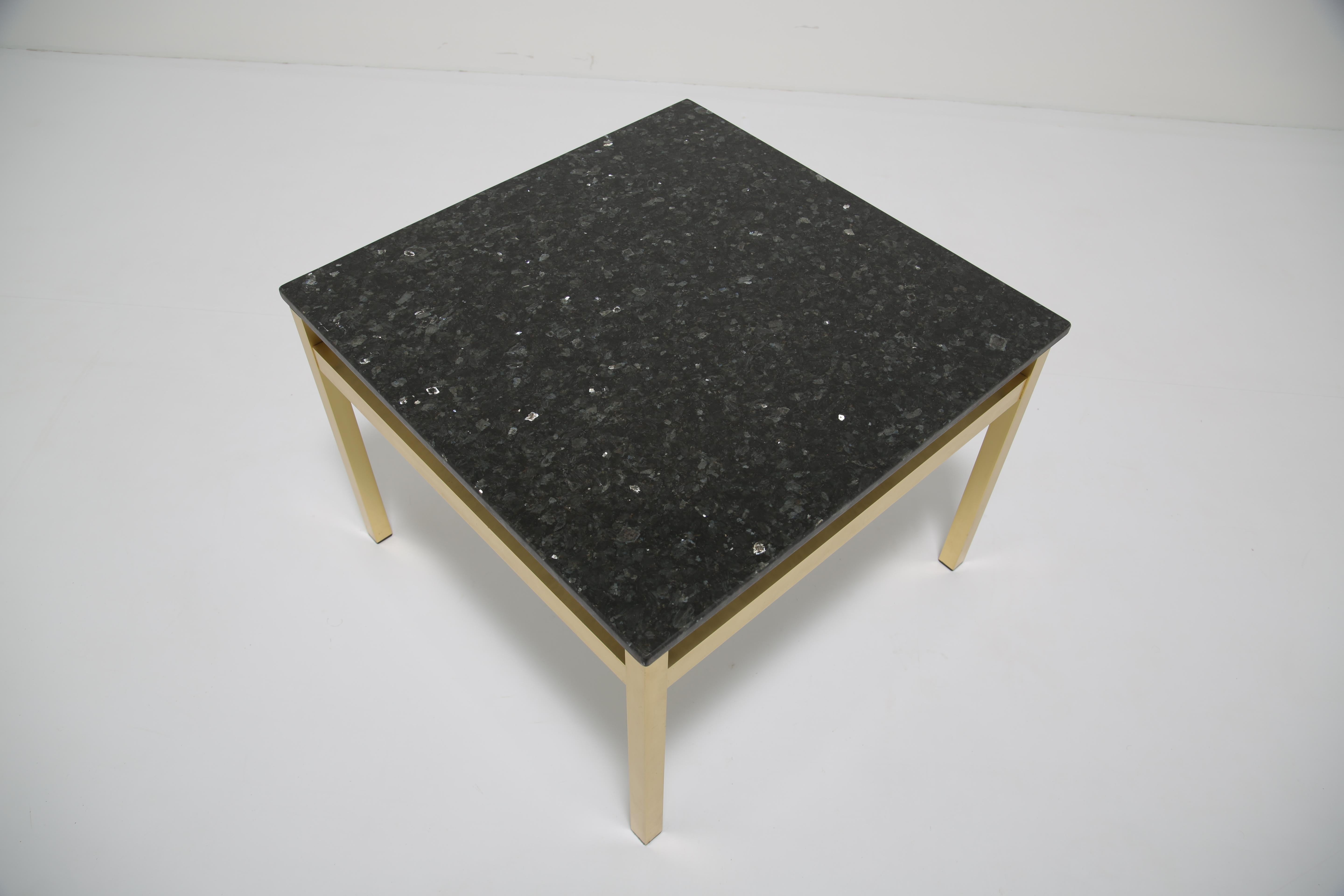 This elegant square table embodies the refined simplicity of mid-century modern design. The top is crafted from black granite with subtle flecks and reflective inclusions that catch the light, creating a surface of depth and sophistication. It rests