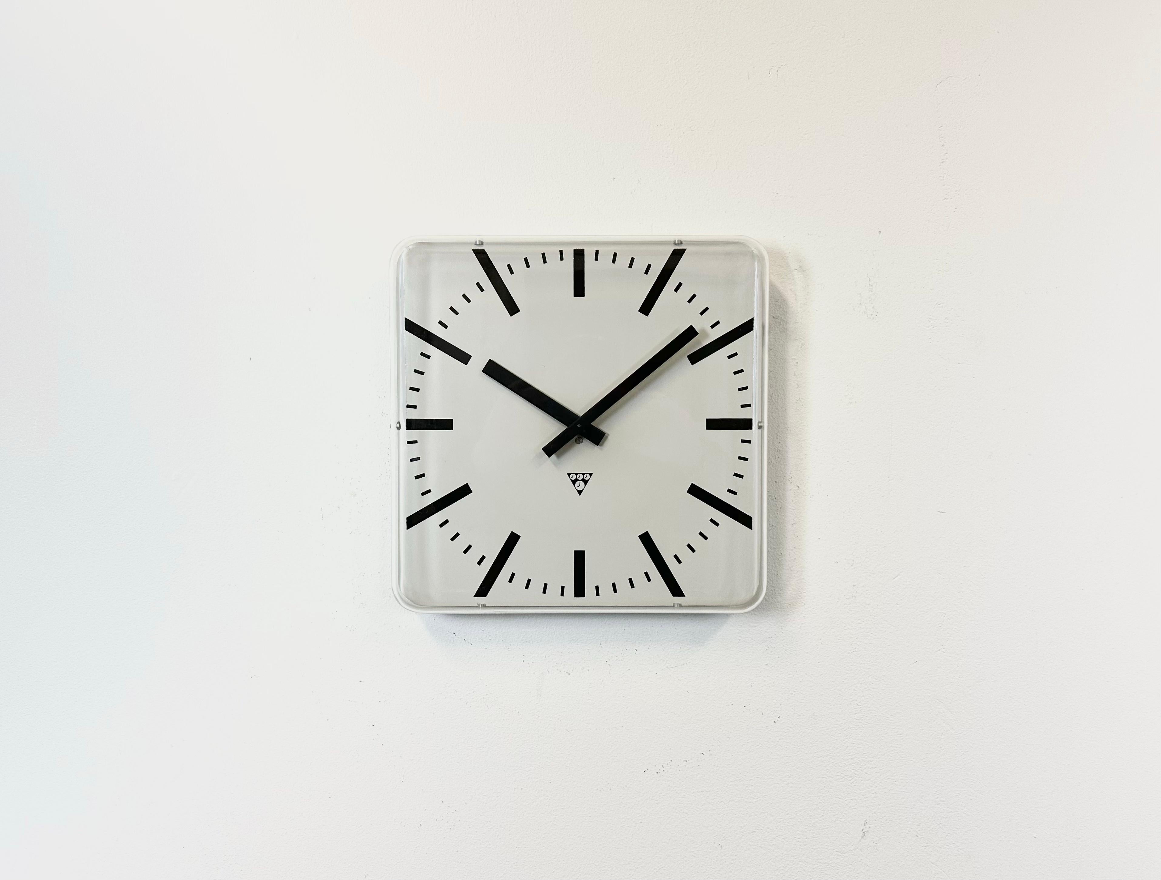 Industrial wall clock produced by Pragotron in former Czechoslovakia during the 1980s. It features a square aluminium dial and a curved plastic clear glass cover. The piece has been converted into a battery-powered clockwork and requires only one