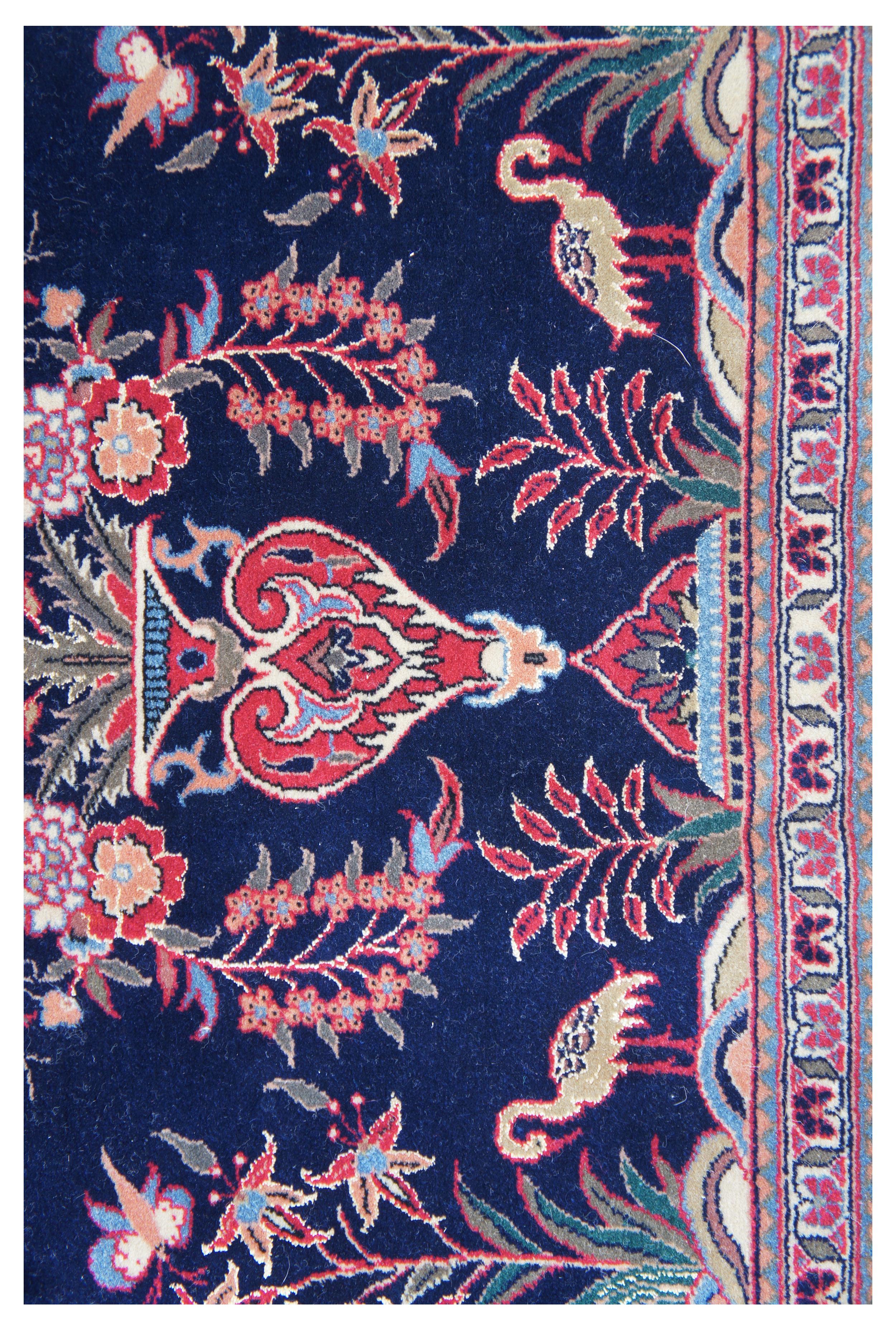 Vintage Persian Oriental vase rug featuring a field of navy blue with a large central vase arrangement of flowers with reds, blues, greens, orange and pink. The piece is accented with butterflies and birds (Flamingo or Stork? / Scissor Tailed