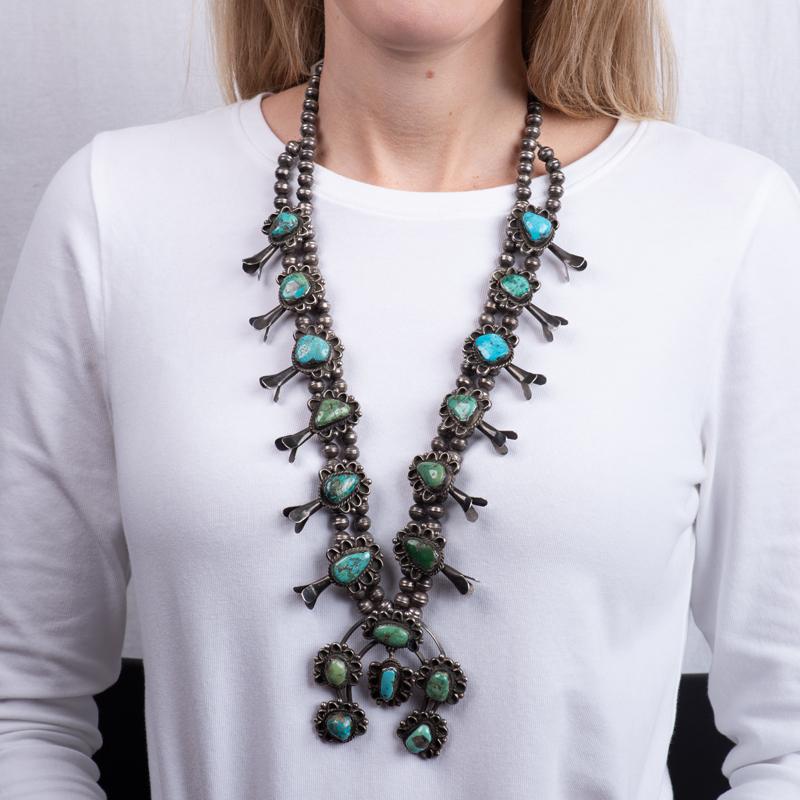 This vintage squash blossom necklace features natural native american green and blue turquoise. The turquoise stones are set in silver on a two row beaded silver necklace. It was hand crafted in the 1960's. 
Measurements: Length approximately 16