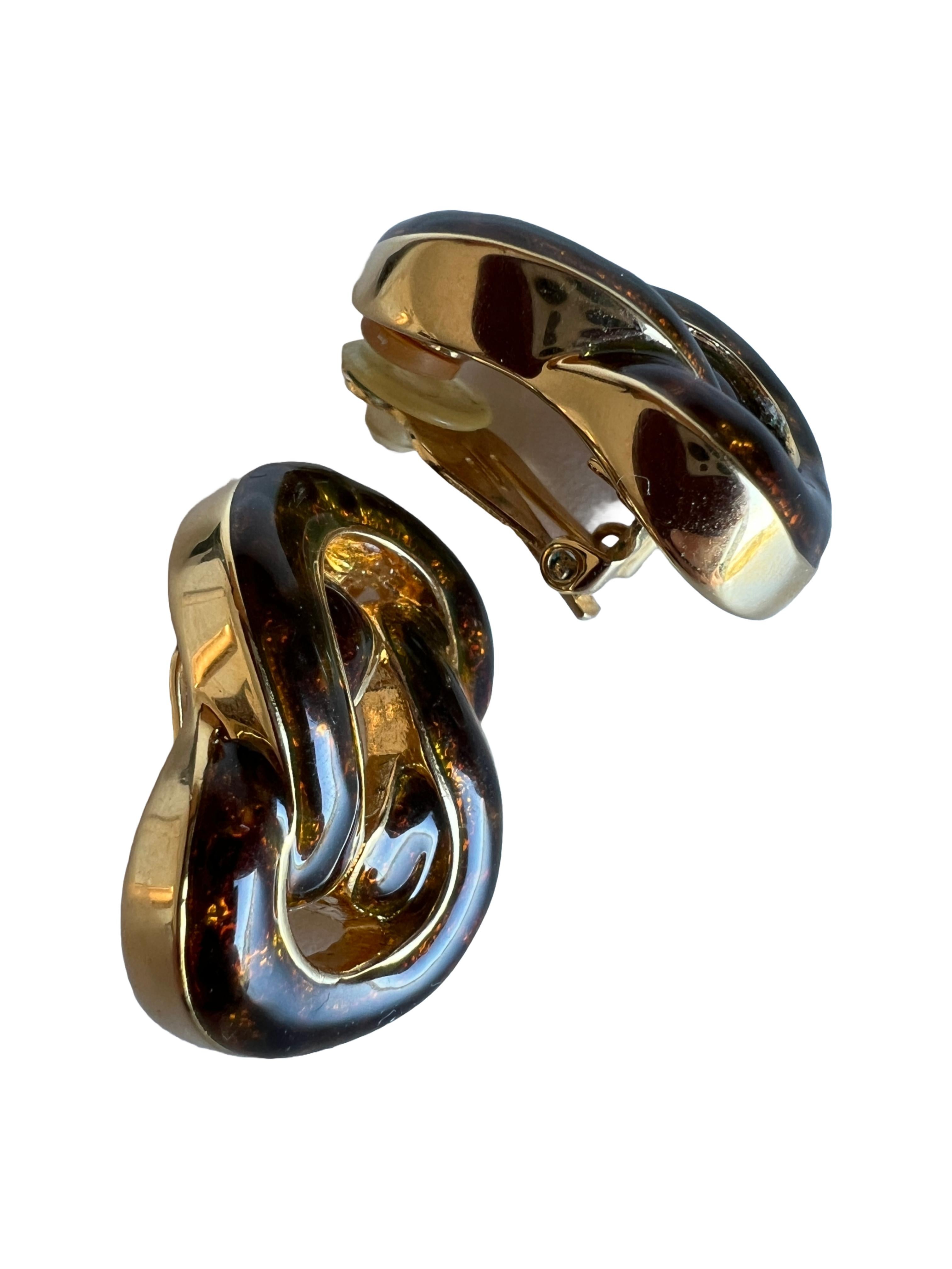 These vintage St. John clip-on earrings feature a beautifully intertwined chain link design, blending gold-tone/plated metal with tortoiseshell-like enamel for a luxurious finish. The sculptural chain link motif is both timeless and bold, making