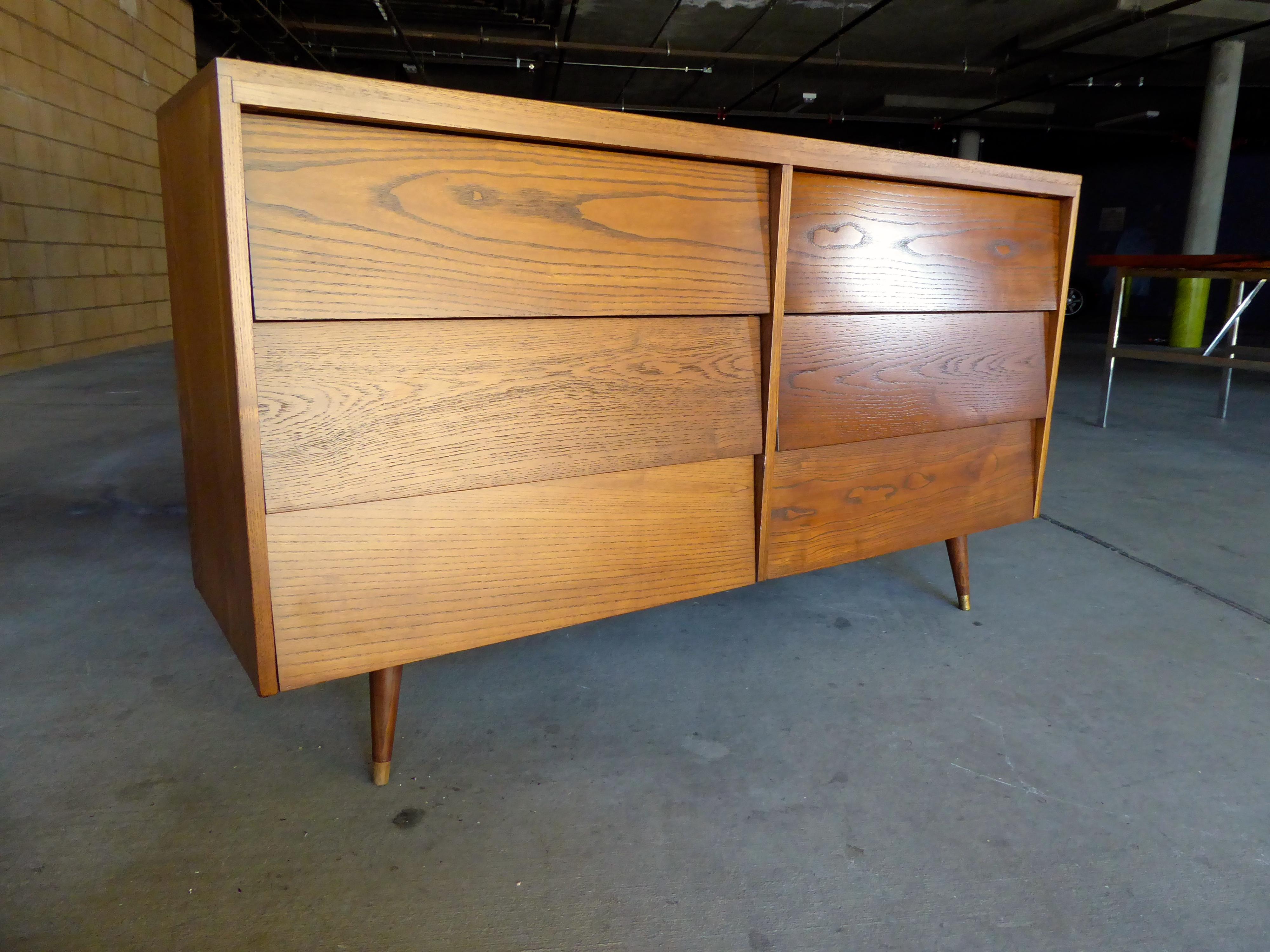 A vintage slat-front stained oak dresser with brass-capped feet, circa 1960s. The chest would be perfect for a second bedroom or for a stylish child's room.
