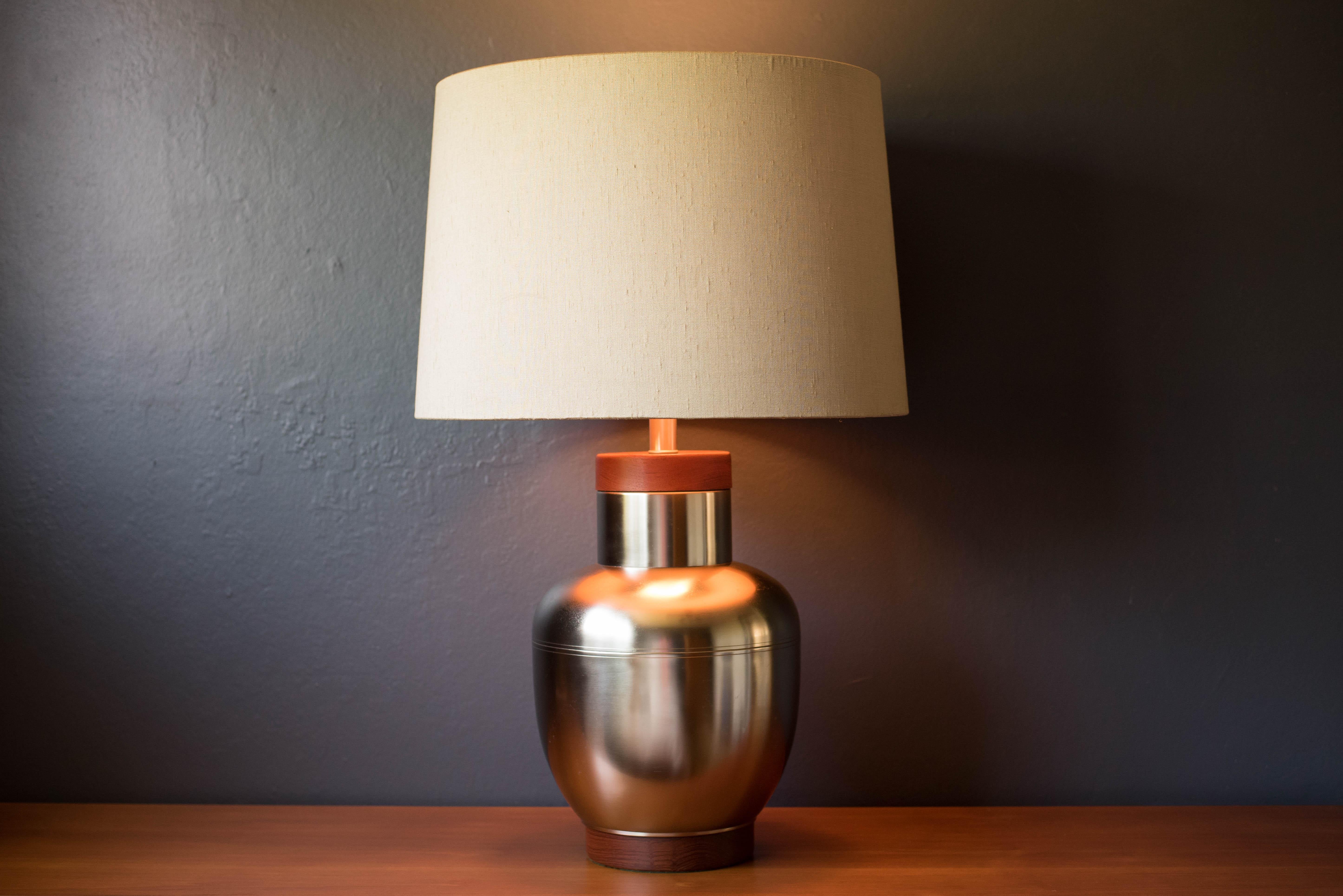 Mid Century Modern table lamp in stainless steel circa 1960's. This classic decorative piece features teak accents and includes a milk glass diffuser. The original linen shade is included. 

Shade: 20