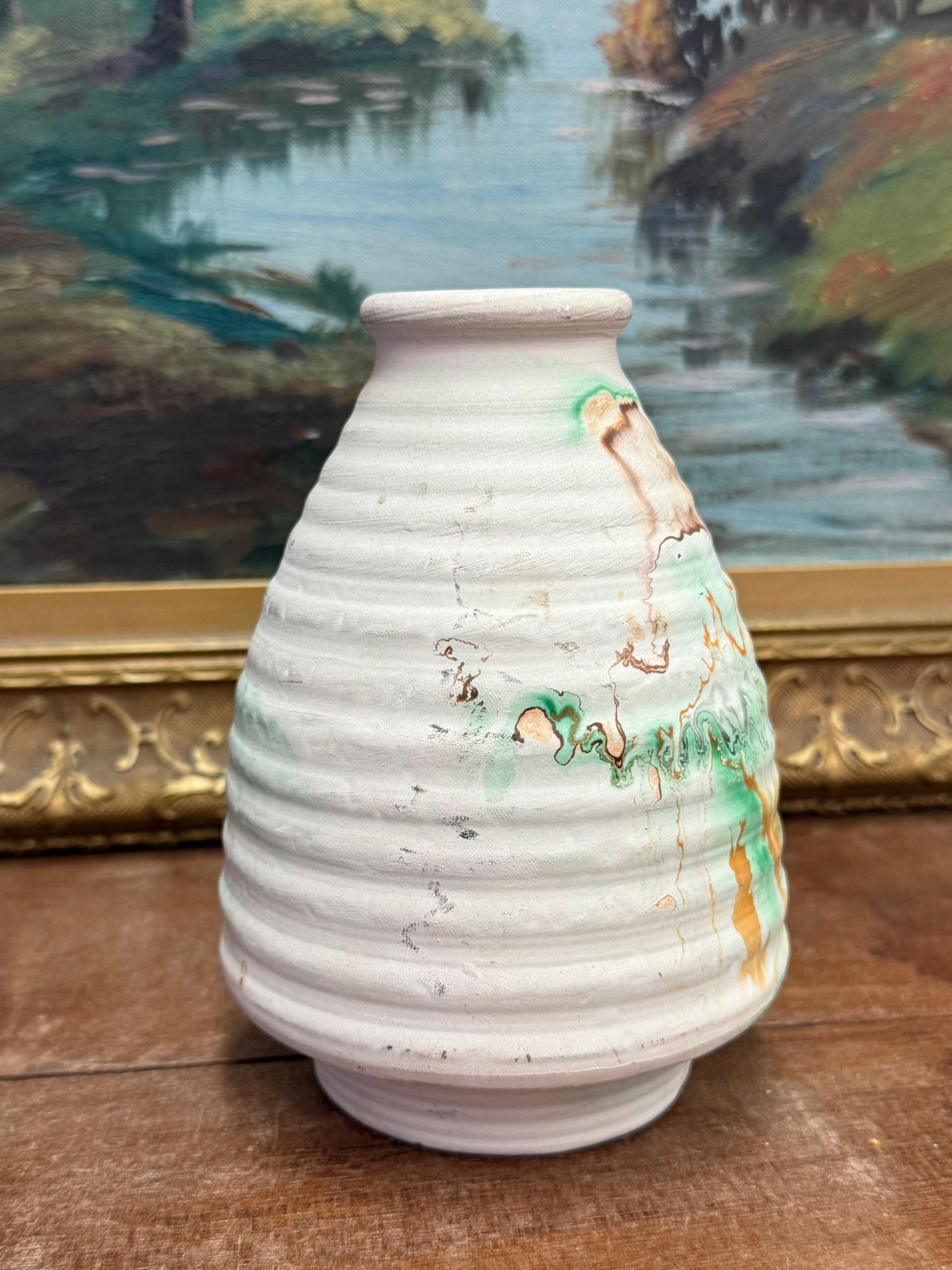 La ceramica è un vaso di ottima fattura con un corpo arrotondato e un collo stretto. Presenta una superficie strutturata con sottili nervature che aggiungono profondità alla sua forma. La palette di colori comprende toni tenui della terra, con