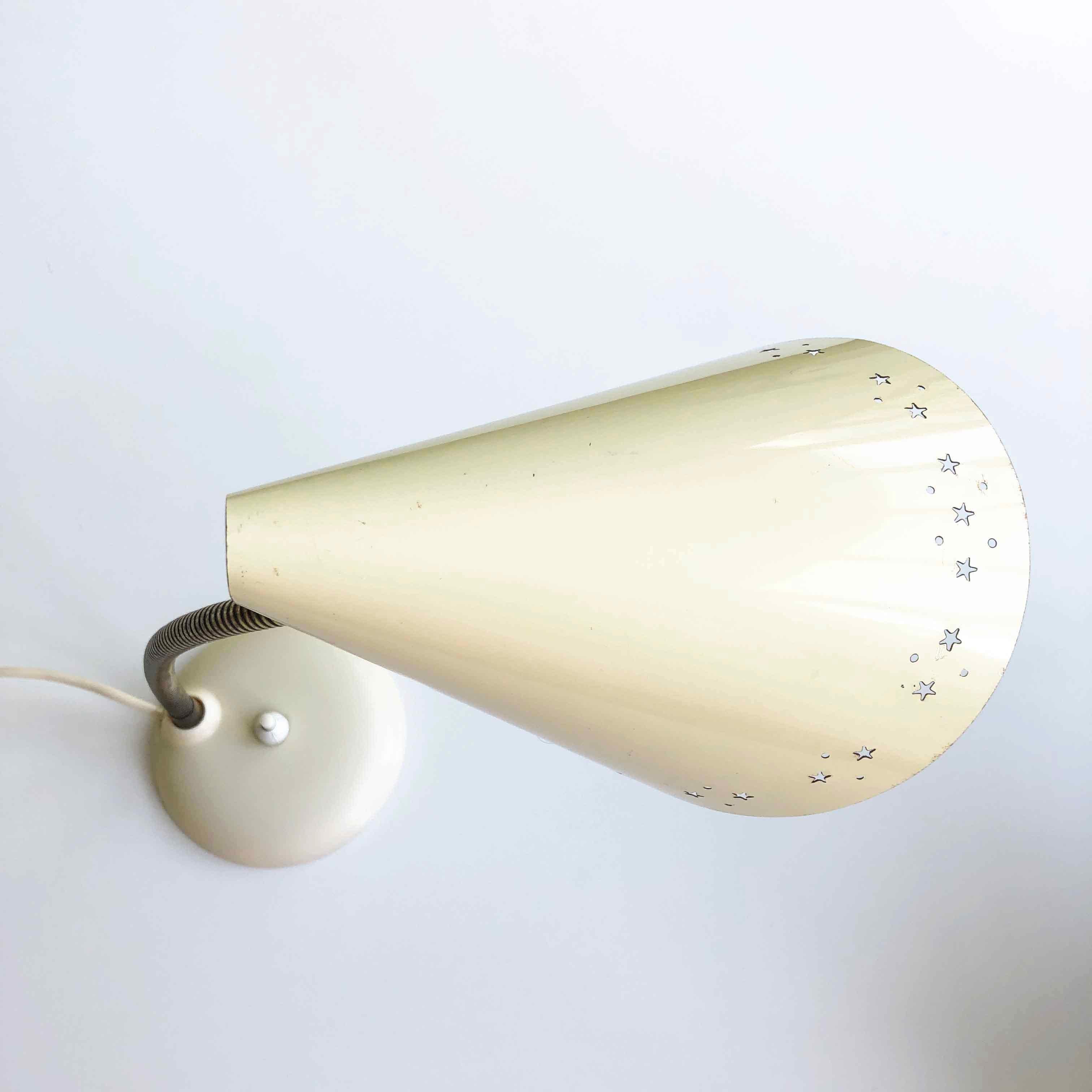 Beautiful star lamp by HoSo Hoffmeister & Sohn from the 1950s.

This desk lamp has a folded conical lampshade in metal. The cream-colored lampshade is perforated all around with stars and round holes. The gooseneck is made of brass and can be