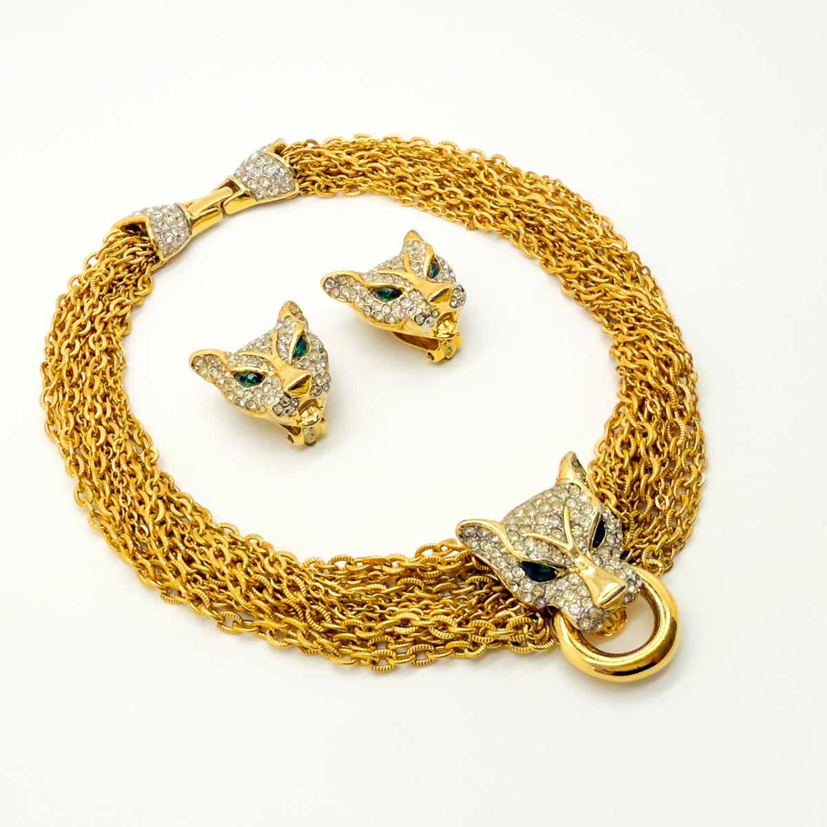 Este conjunto vintage de collar de cadena y pendientes Big Cat es un conjunto excepcional que refleja el atrevido glamour de las legendarias joyas de pantera de Cartier. Fabricada en metal con un rico baño de oro, la atención al detalle es notable,