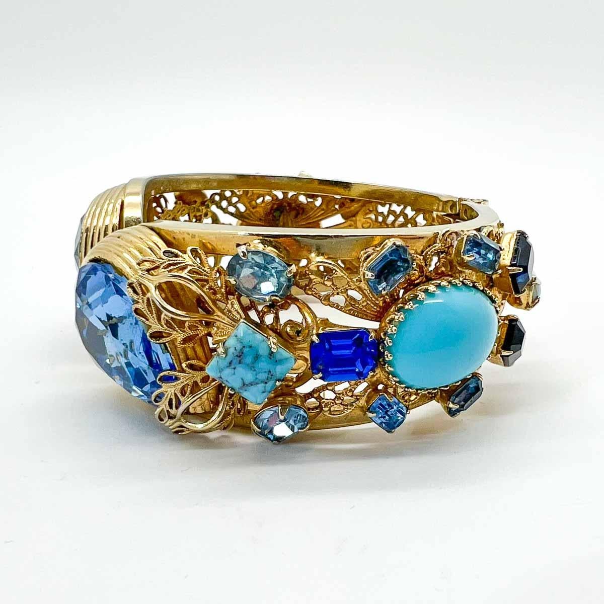 A beautiful statement vintage blue teardrop clamper bracelet. Featuring a myriad of fancy cut stones including opulent cabochons, in blue hues and turquoise shades set amongst a filigree backdrop. The large teardrop crystals a particularly wonderful