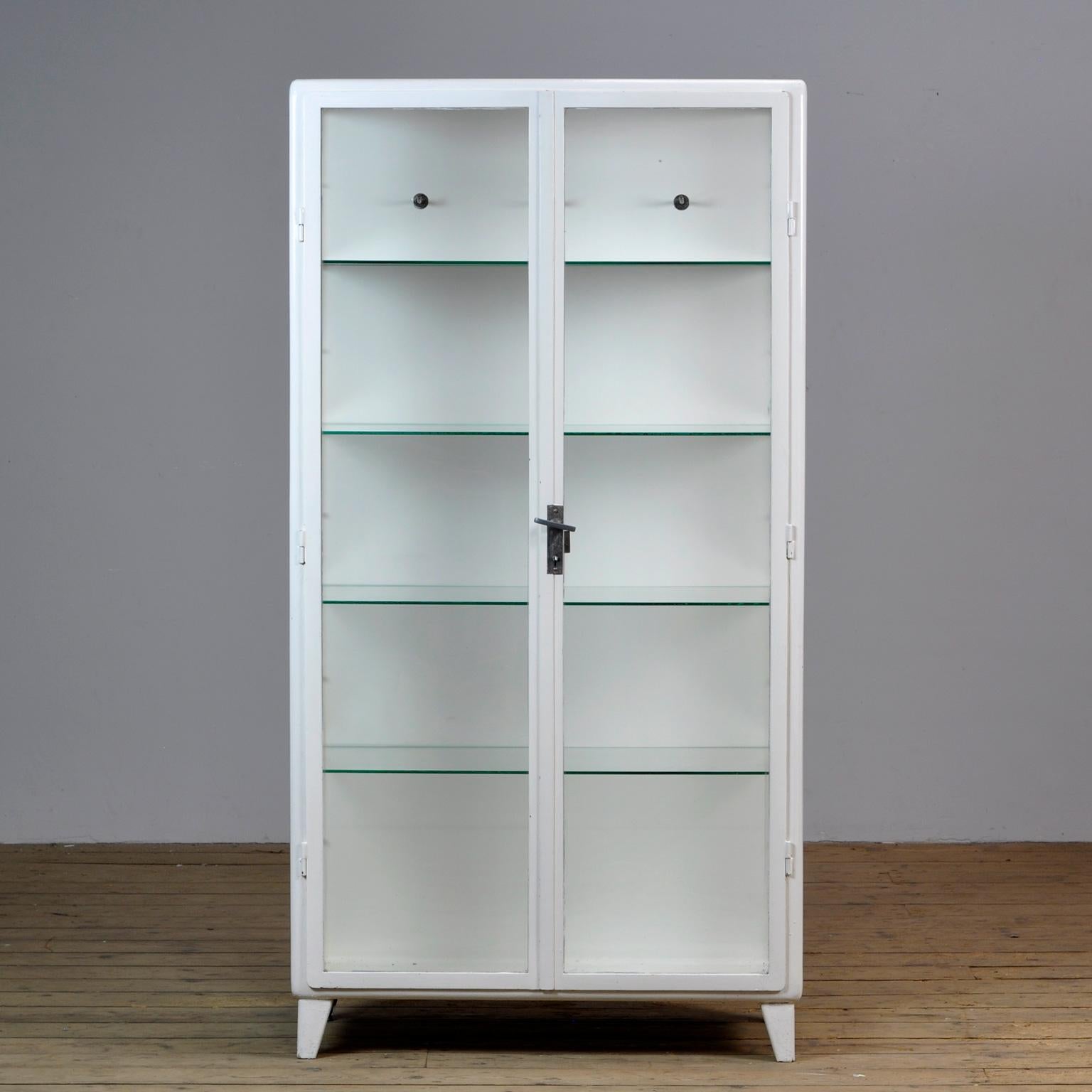 Polish medical cabinet, produced in the 1960's. Made of iron and the original antique glass. Elegant design with rounded corners. On the inside three clothes hooks and 4 glass shelves. 