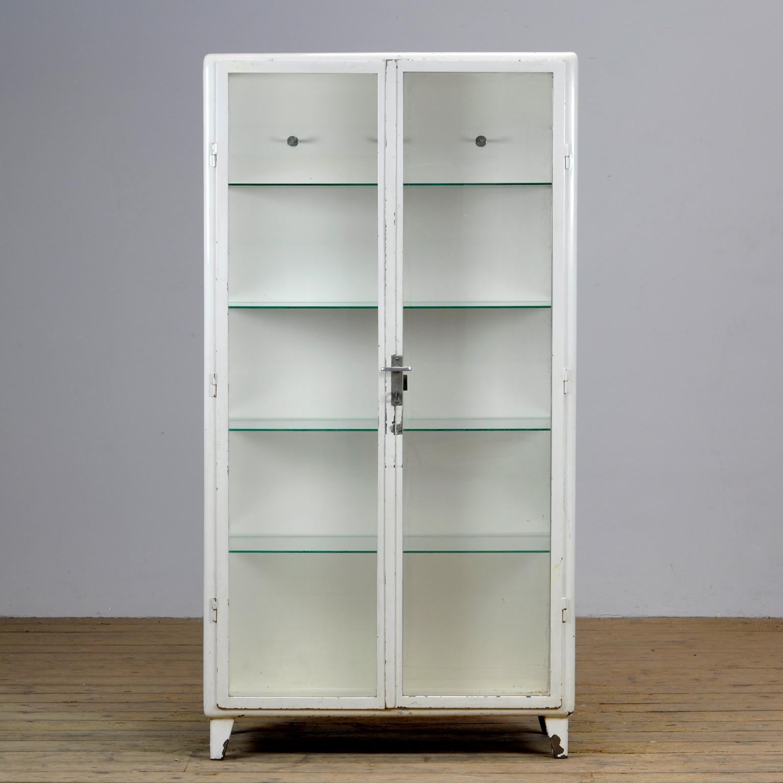 Polish medical cabinet, produced in the 1960's. Made of iron and the original antique glass. Elegant design with rounded corners. On the inside three clothes hooks and 4 glass shelves. 