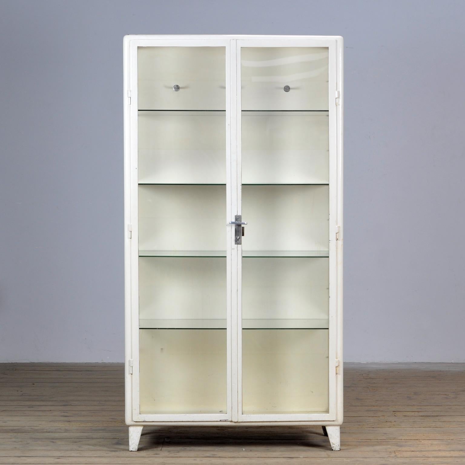 Polish medical cabinet, produced in the 1960’s. Made of iron and the original antique glass. Elegant design with rounded corners. On the inside three clothes hooks and 4 glass shelves. 