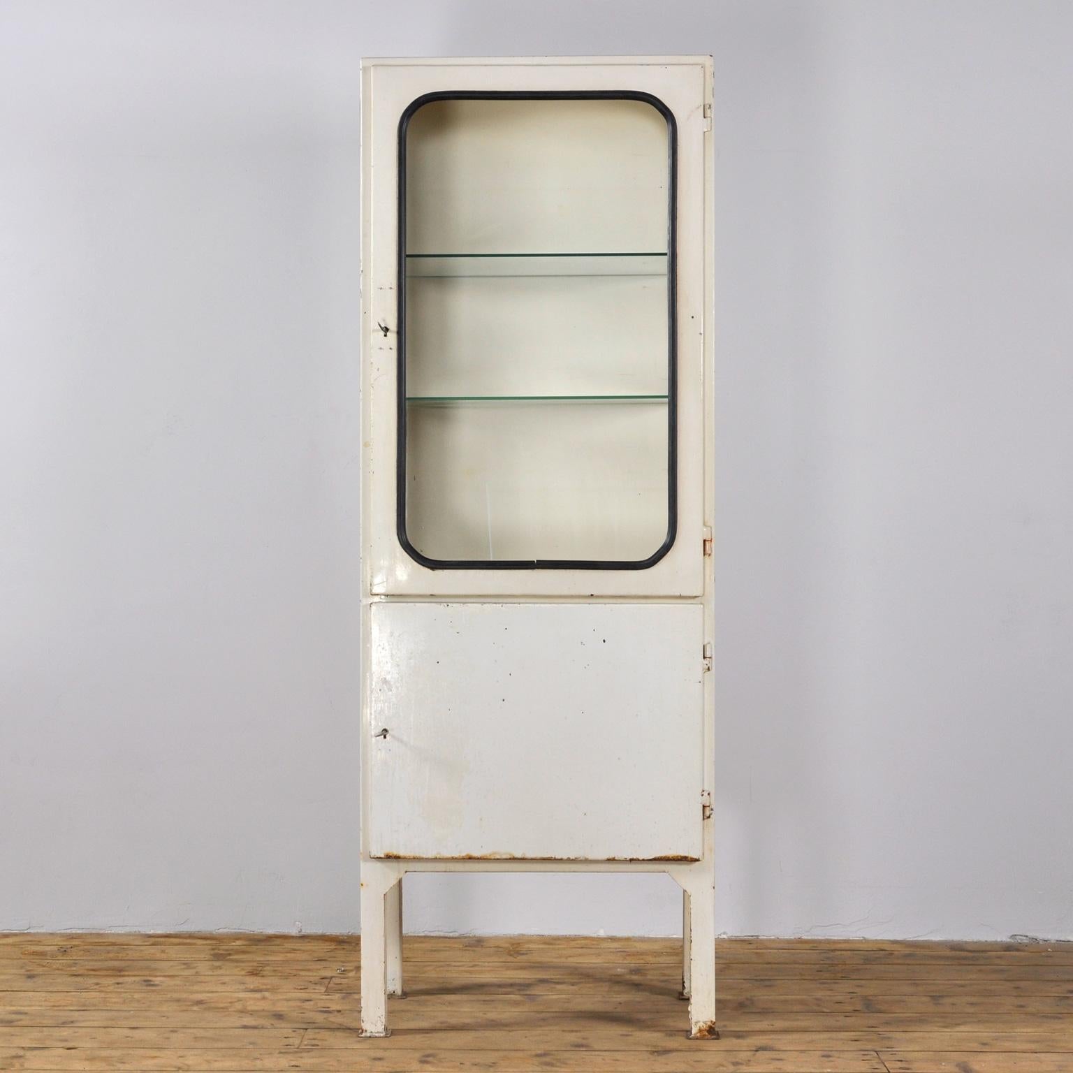 This medical cabinet was designed in the 1970s and was produced circa 1975 in Hungary. It is made from iron and antique glass with new glass shelves. The glass is held by a black rubber strip. The cabinet features two adjustable glass shelves and