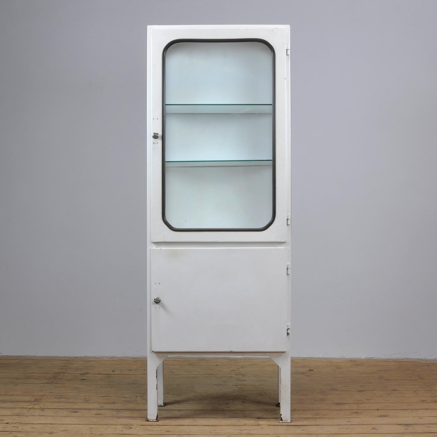 This medical cabinet was designed in the 1970s and was produced circa 1975 in Hungary. It is made from iron and antique glass with new glass shelves. The glass is held by a black rubber strip. The cabinet features two adjustable glass shelves and