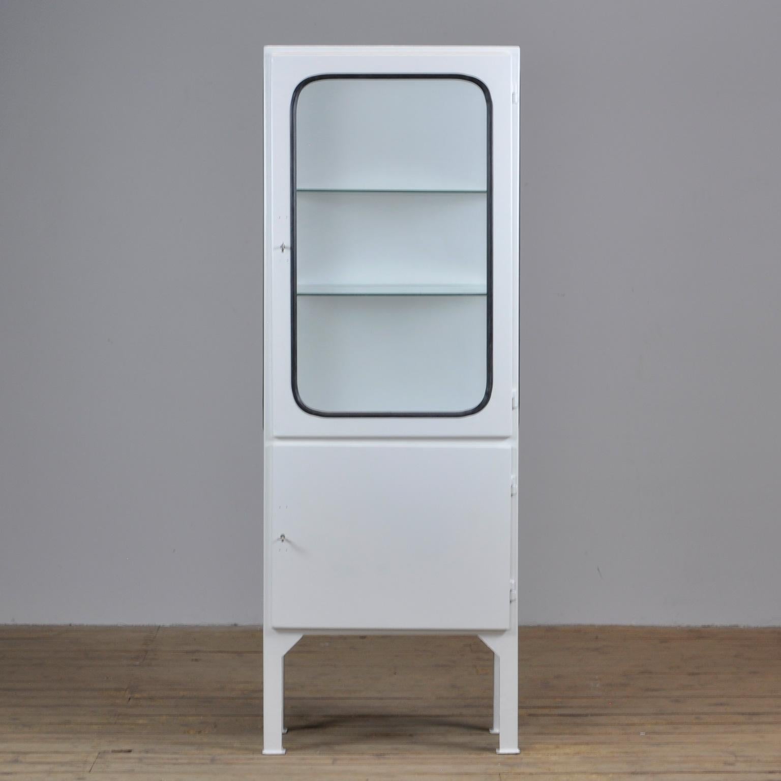 This medical cabinet was designed in the 1970s and was produced, circa 1975 in Hungary. It is made from iron and antique glass with new glass shelves. The glass is held by a black rubber strip. The cabinet features two adjustable glass shelves and