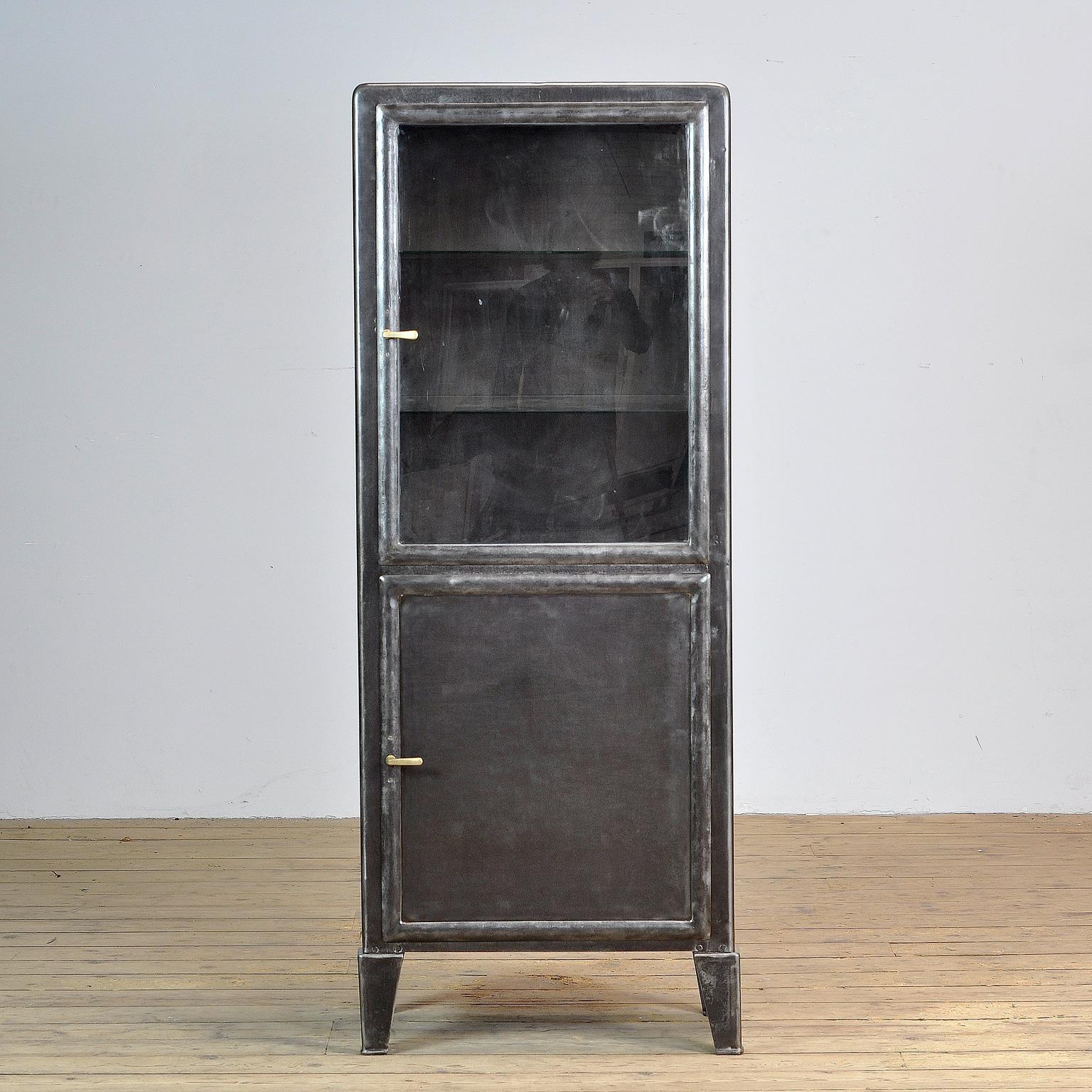 This medical cabinet was produced in the 1930s in Hungary. The cabinet is made from iron and glass with brass handles. The cabinet has been stripped from its paint, polished and treated for rust. It features four glass shelves. The shelves in the