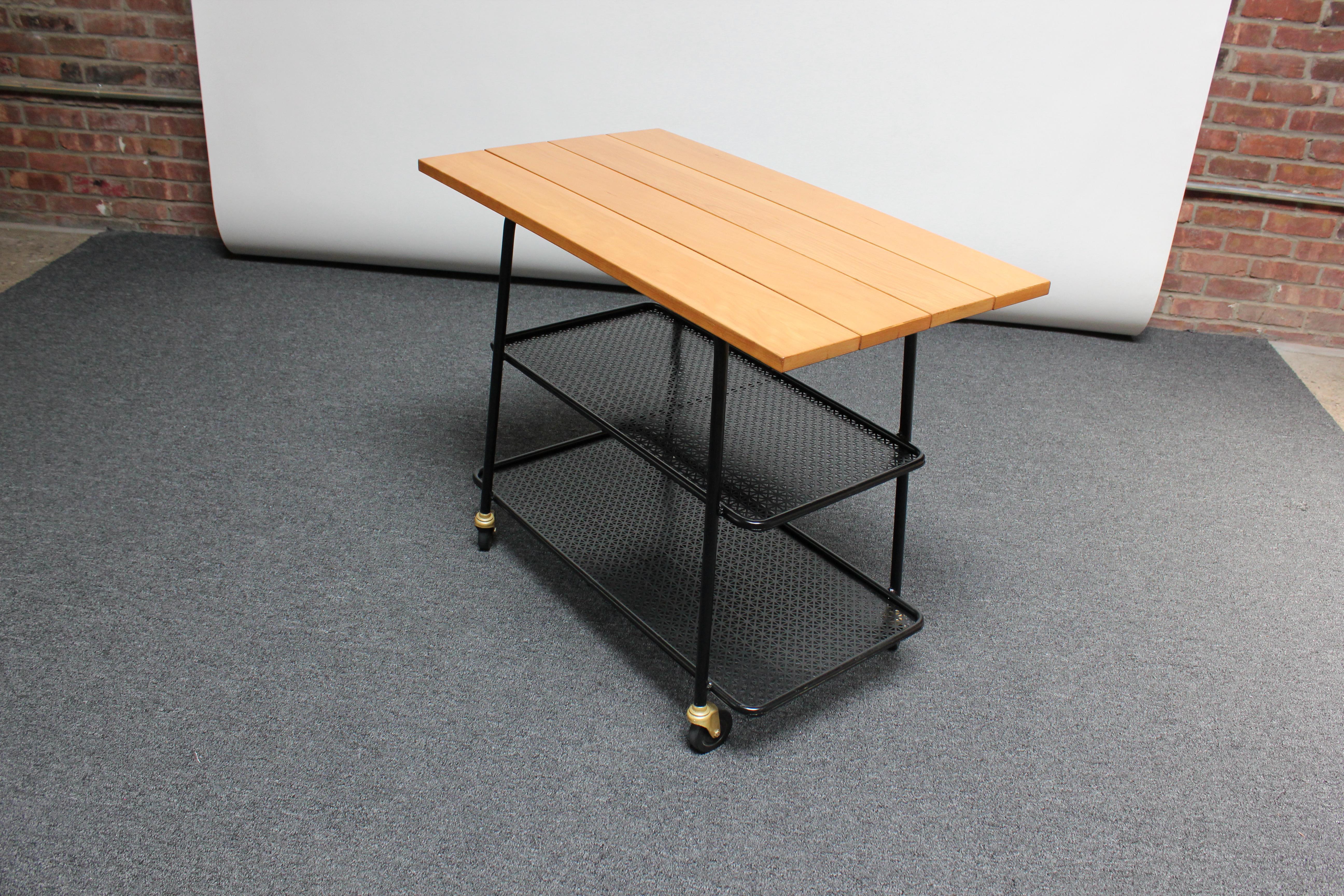 Mid-century bar cart / tea trolley featuring two perforated steel tiers and a solid maple plank surface.
The maple adds a nice contrast to the black painted steel.
Maple has been refinished, and the piece is in excellent, vintage condition; only