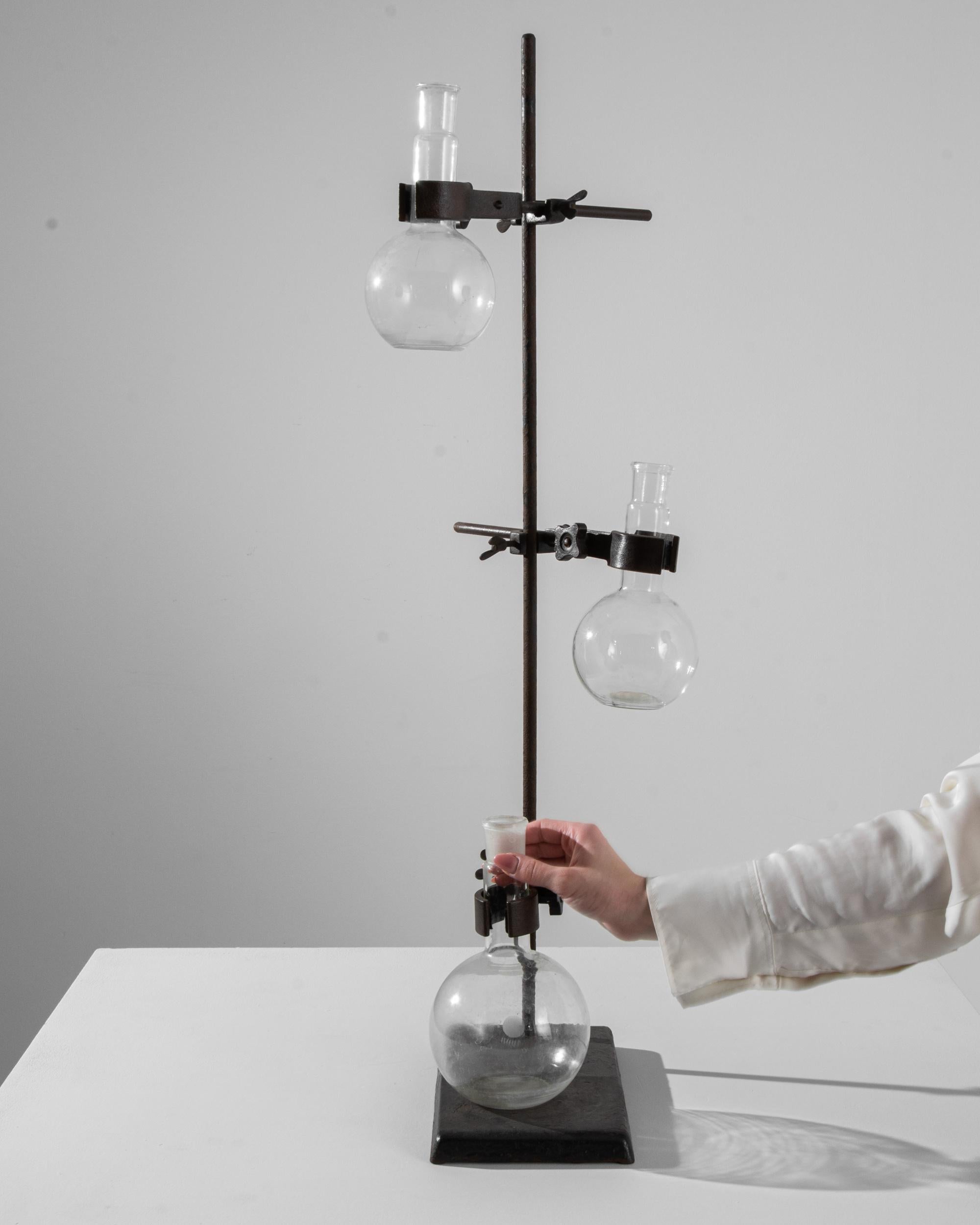 An intriguing and unique accent, this vintage lab-ware stand holds three round-bottomed flasks. Once used as a tool for conducting laboratory analysis or experimentation, the globe-like spheres glint with the crystal clarity of borosilicate. The