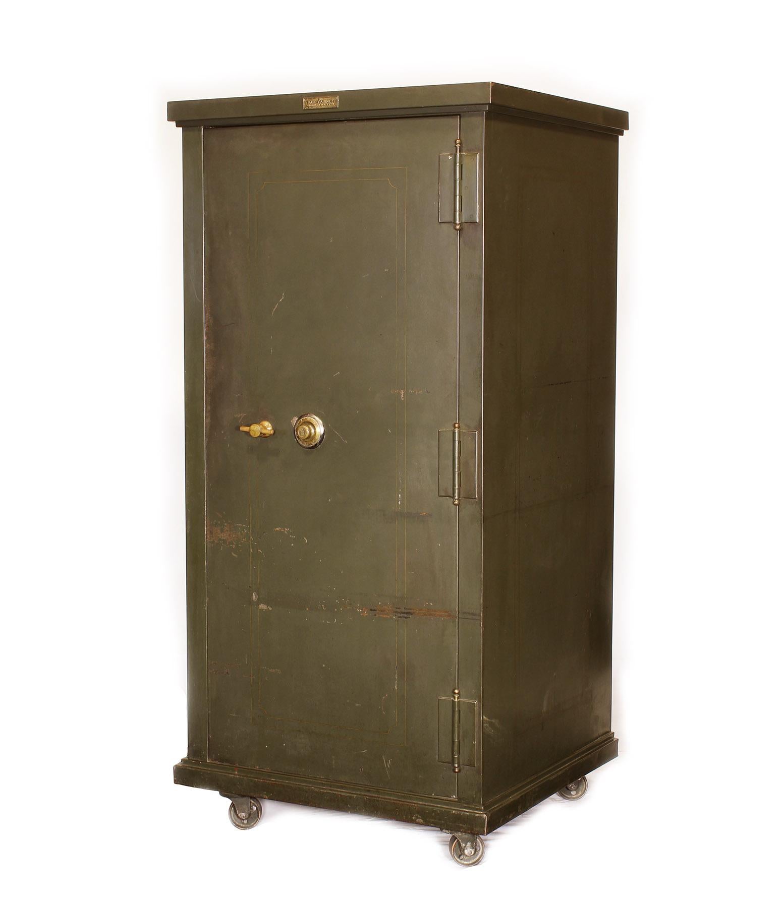 Vintage steel bank / gun safe made by The Safe-Cabinet Co. Features two drawers, adjustable shelves, one storage compartment, four swivel castors and brass hardware. Three labels on safe. 