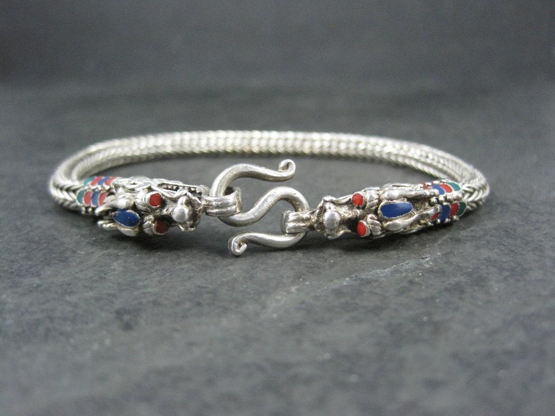 This gorgeous vintage dragon bracelet is sterling silver with enamel detailing.

The head of the dragons measure 5/16 wide by 3/8 of an inch tall.
The woven wheat chain measures 5mm wide.
8 total wearable inches

Weight: 27.3 grams

Marks: 925 (3