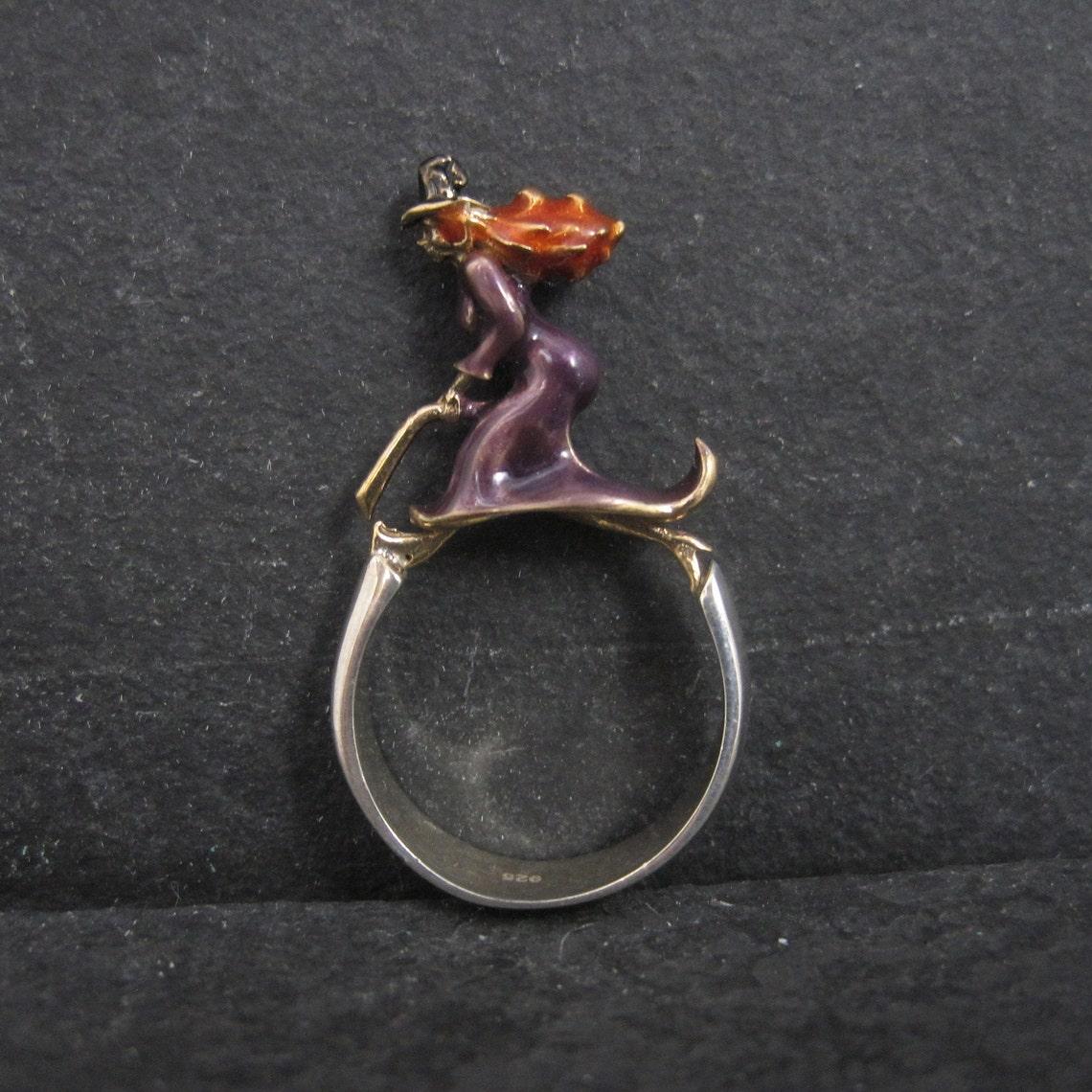 This gorgeous ring is sterling silver.
It features a beautifully detailed vermeil witch with delicate enamel detailing.

The face of this ring measures 1/4 of an inch wide. It sits 18mm off the finger.
Size: 7 1/2
Marks: 925

Condition: Excellent
