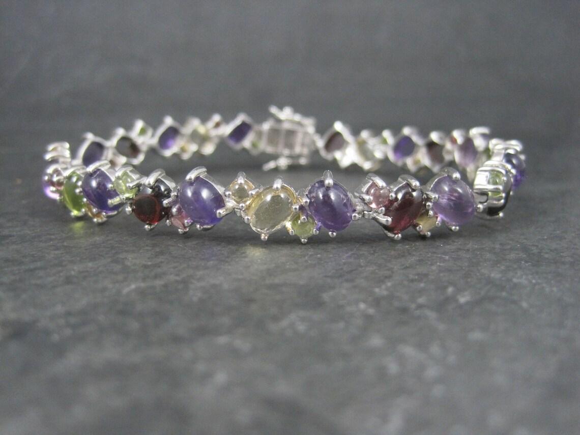 This gorgeous estate bracelet is sterling silver.
It features cabochon cut garnets, citrines, peridot, amethysts and pink tourmalines.

Measurements: 3/8 of an inch wide, 7 3/4 wearable inches

Condition: Phenomenal
