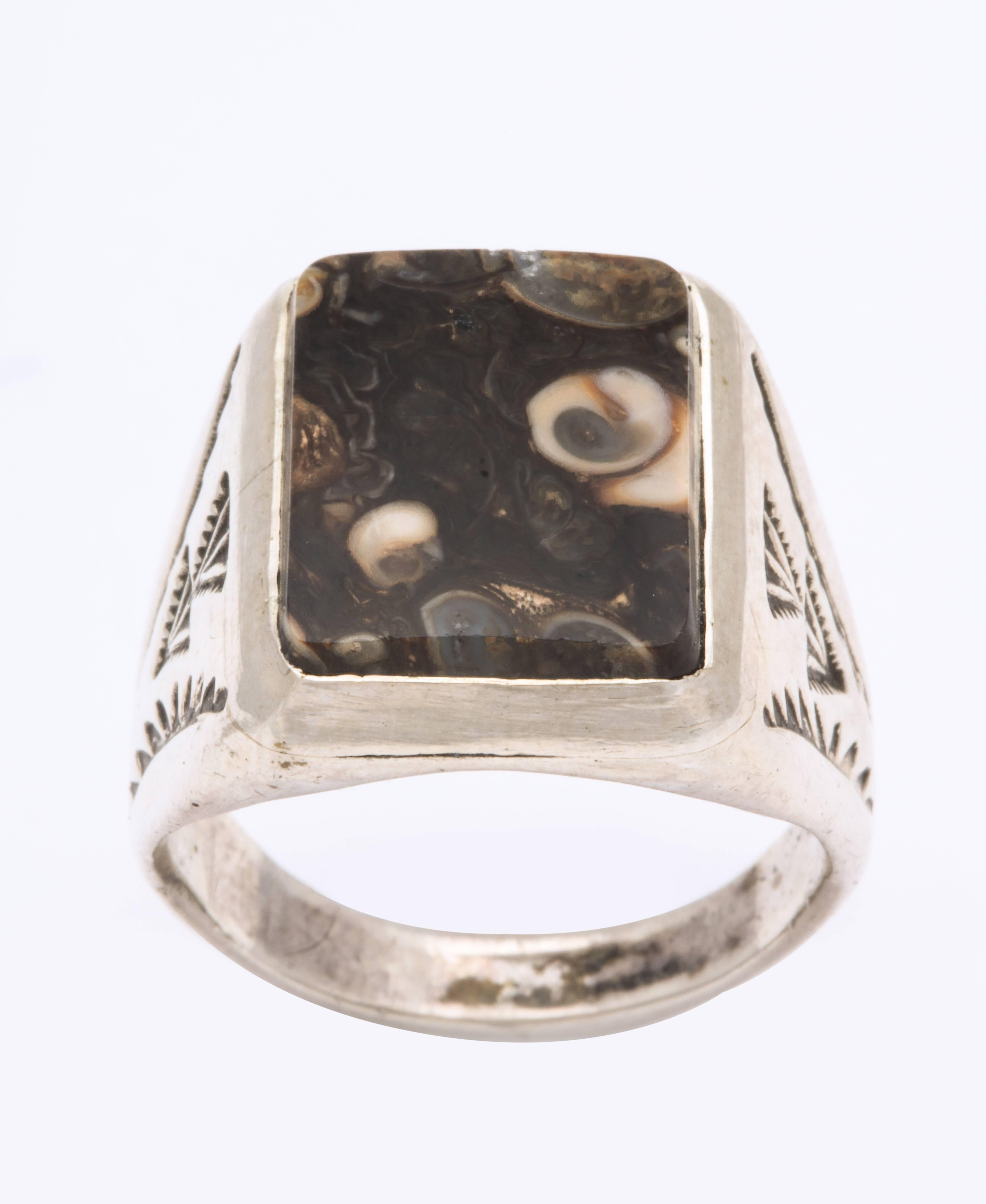 Fabriquée vers 1940, cette belle bague en argent sterling coulé est sertie d'une pierre fossilisée unique. Les larges épaules sont gravées à la main de flèches stylisées. Cette bague forte et intéressante convient à un homme ou à une femme.  Taille