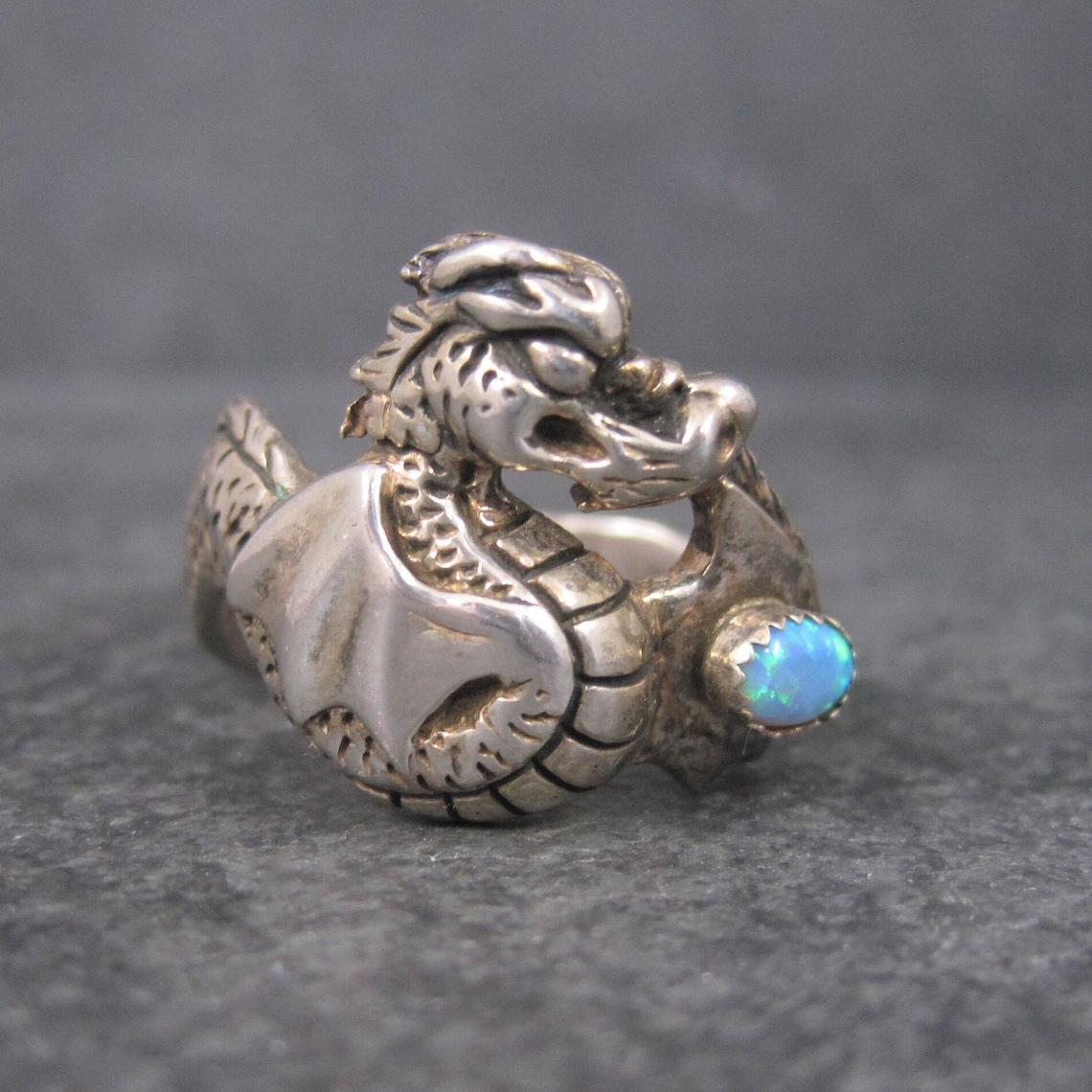 This beautiful dragon ring is sterling silver.
It features an oval cut 6x4mm created opal gemstone.

The face of this ring measures 3/4 of an inch north to south.
Size: 13

Marks: $, 925

Condition: Excellent with minor patina