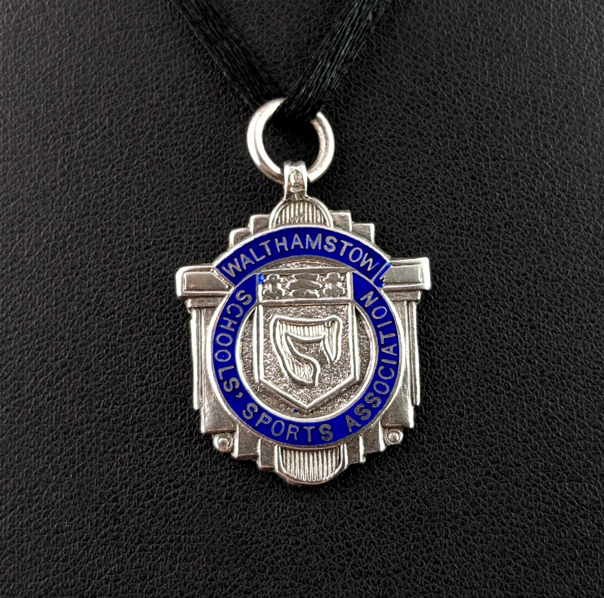 An attractive vintage sterling silver and enamel fob pendant.

It is an unusual shaped piece with a column design, the fob has a blue enamel circular rim with lettering picked out in silver, Walthamstow School Sports Association and has a central