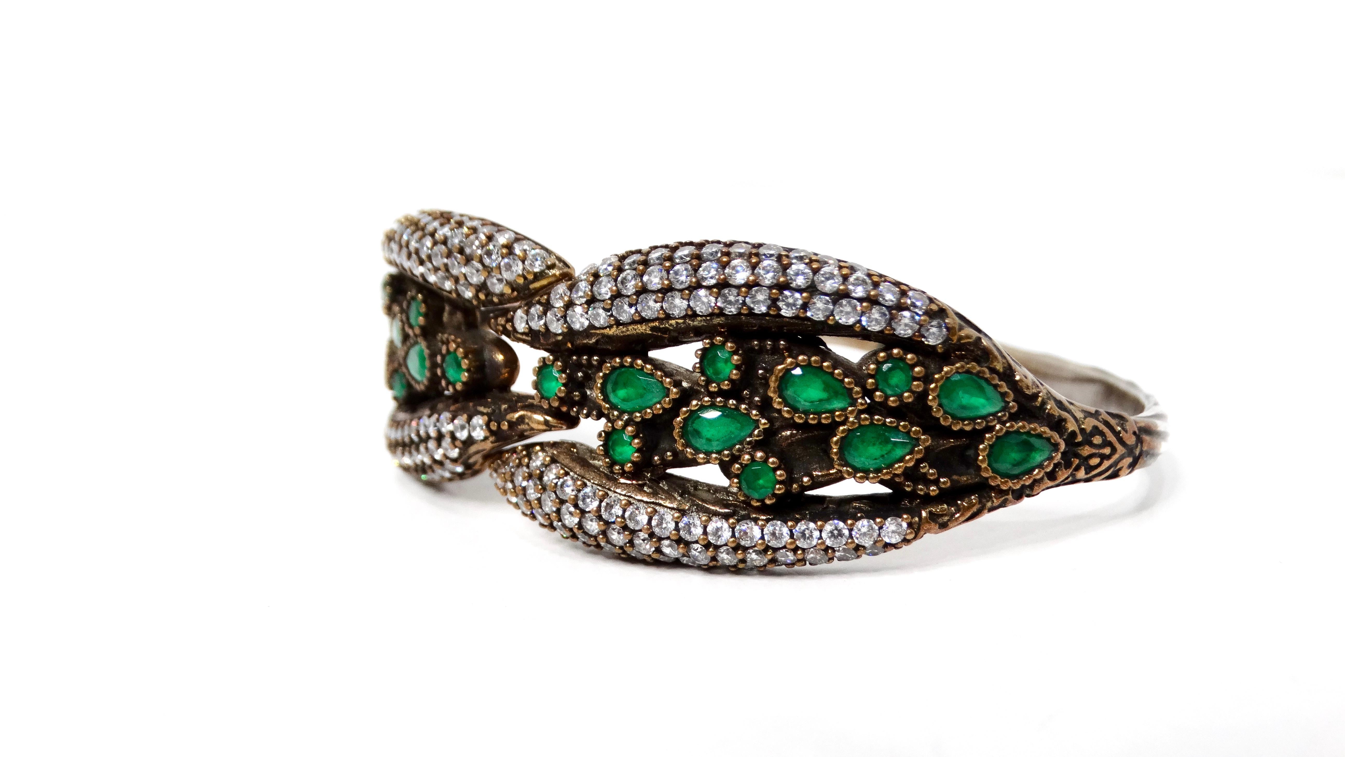 This Vintage Sterling Silver Clamper Bracelet With Green Stone & Crystal Accents is a true showstopper, boasting an exquisite blend of opulence and whimsy. The sterling silver base, adorned with ornate details and set with sparkling crystal