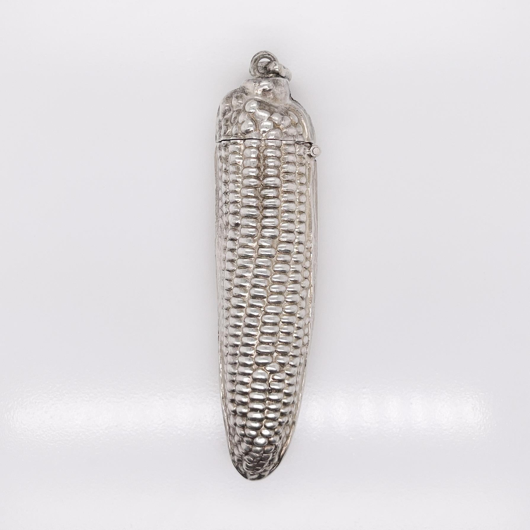 A silver pendant snuff box.

In the form of a half husked corn on the cob with rows of corn grains and the veining of the leaves in high relief.

Fixed with a jump ring for attaching to a chatelaine or to wear as a pendant in a necklace.

Simply a